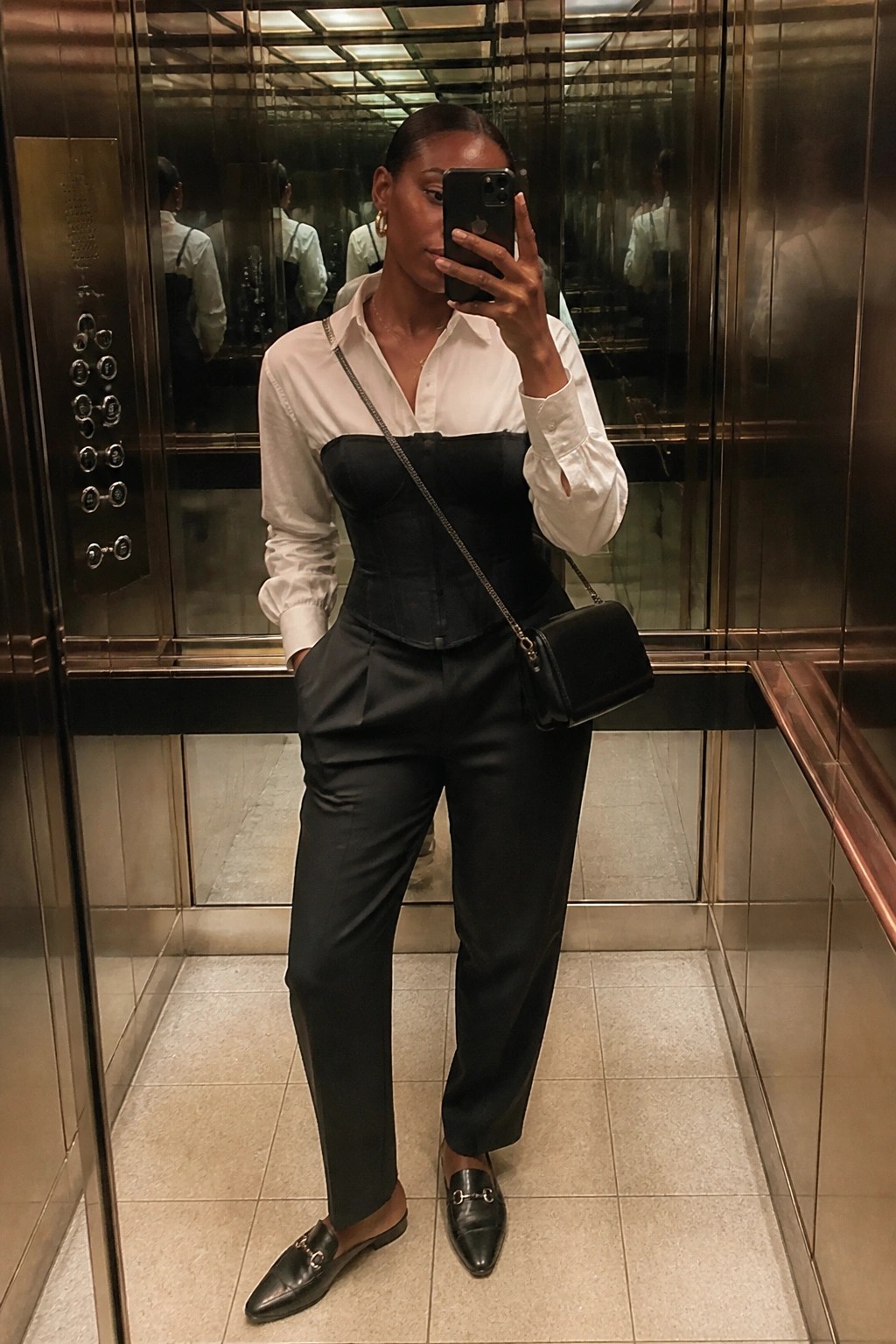 Woman in white shirt and black corset taking mirror selfie in elevator