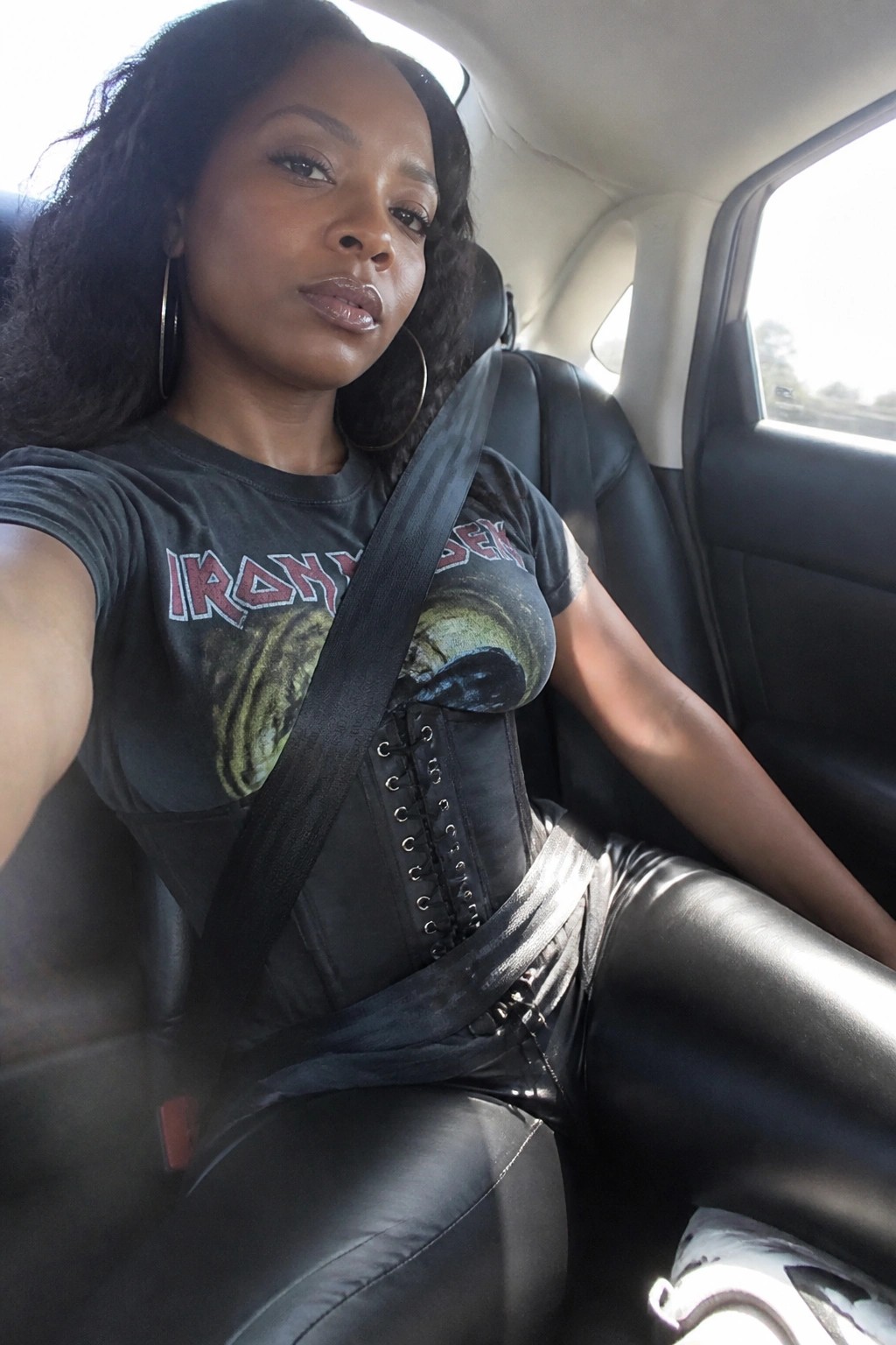 Woman in Iron Maiden shirt and corset with seatbelt in car seat