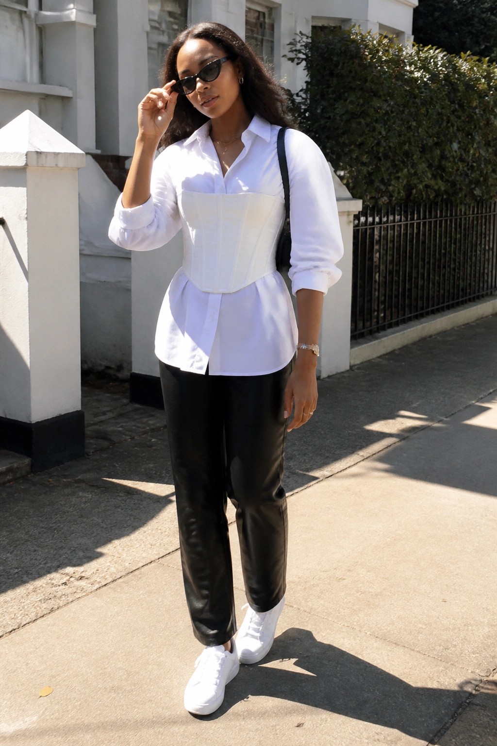 Woman in white corset over shirt, black leather pants, and white sneakers outdoors