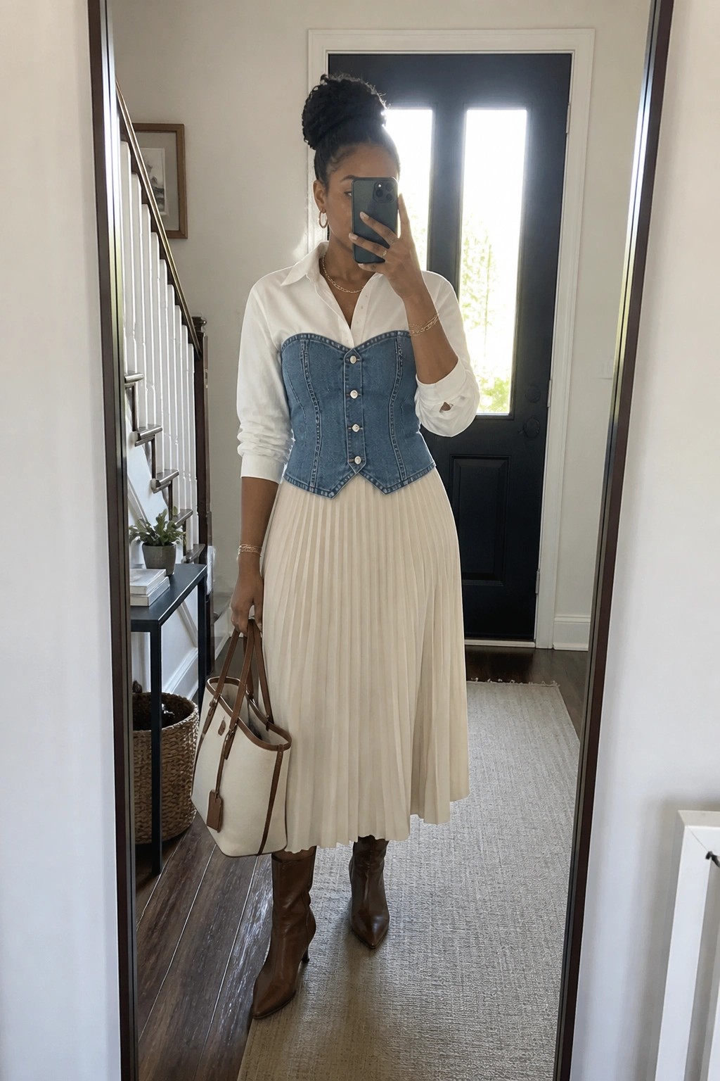 Woman in white shirt and denim corset with pleated skirt holds tote bag for mirror selfie.