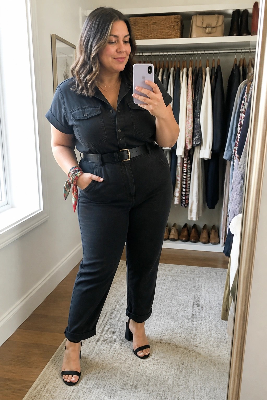 Woman in black denim jumpsuit taking mirror selfie in walk-in closet