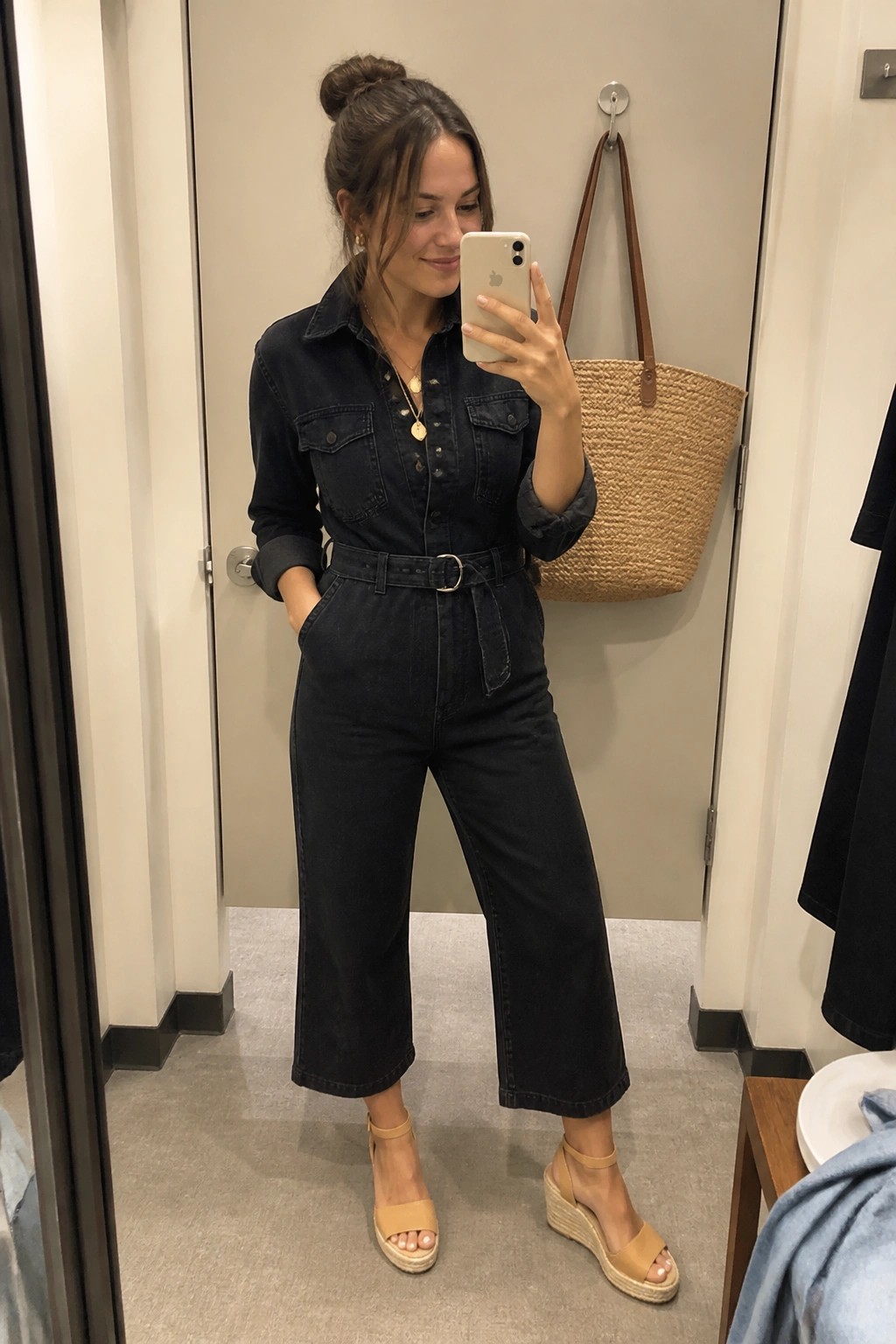 Woman in dark denim jumpsuit and tan wedge sandals taking mirror selfie.