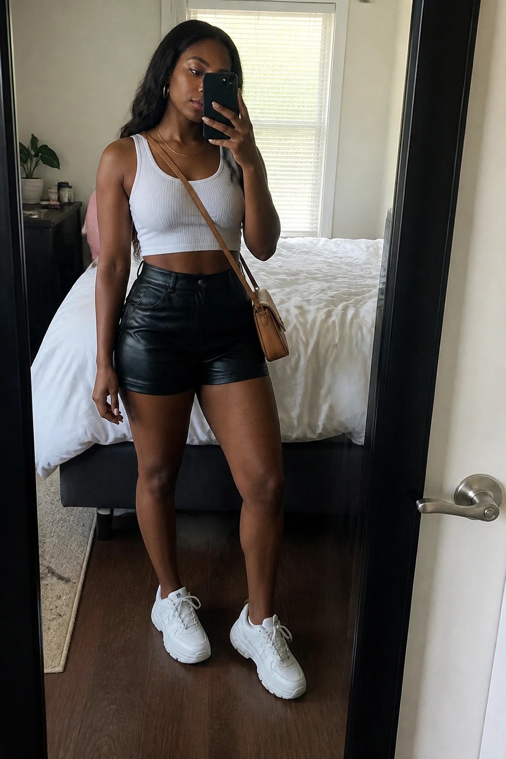 Woman in white crop top and black shorts taking bedroom mirror selfie.