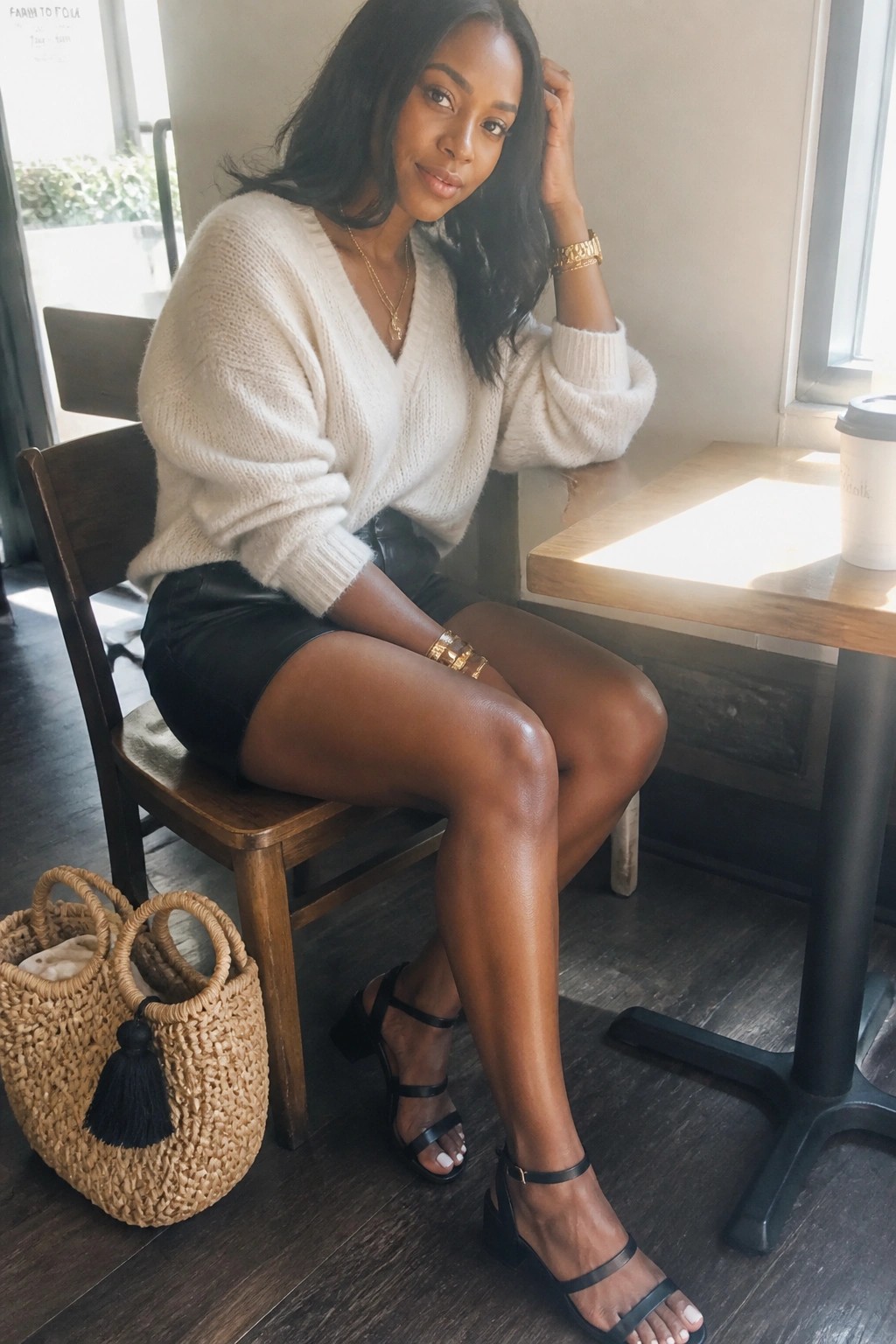 Woman in white knit sweater and black leather skirt at cafe with woven bag