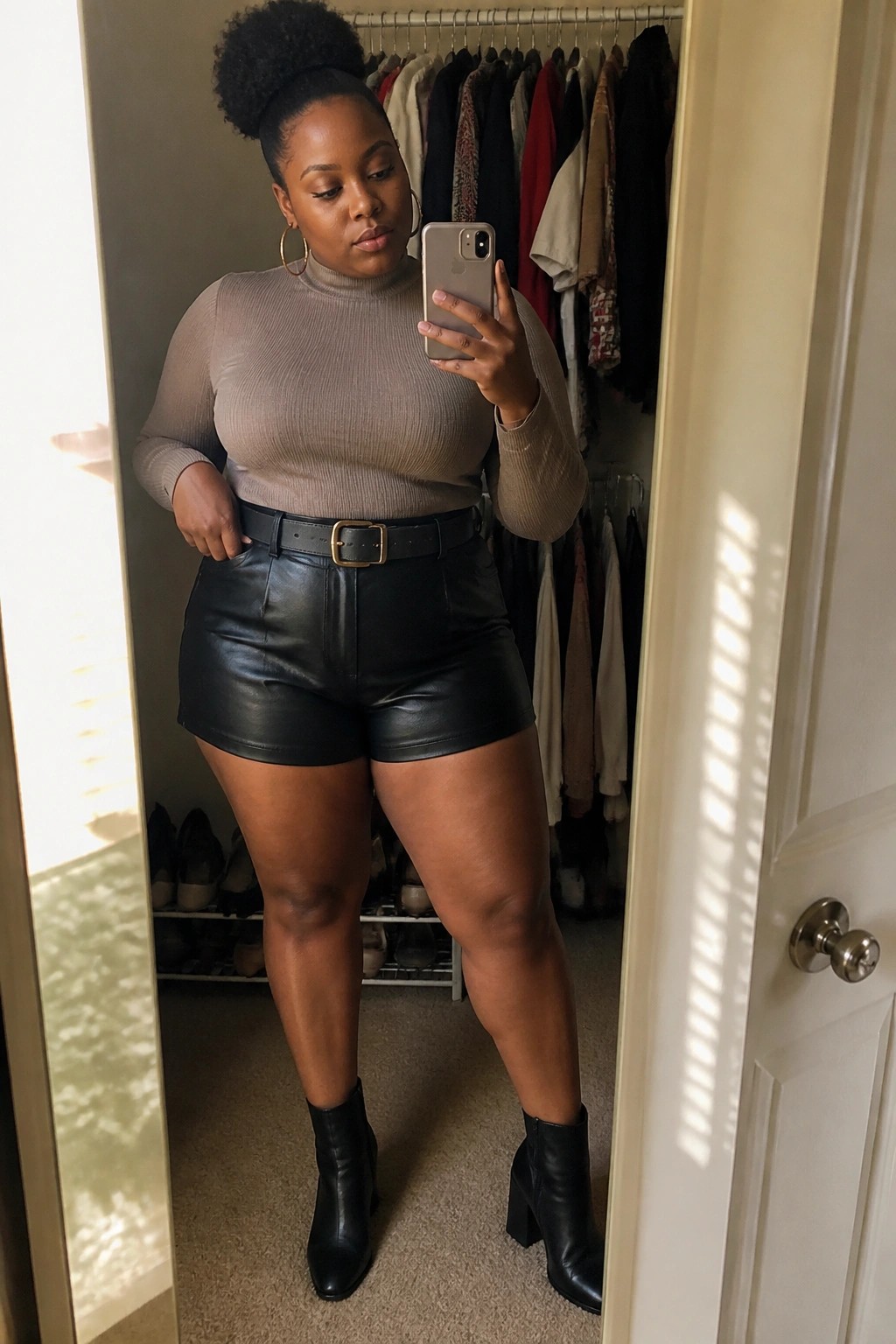 Woman in beige turtleneck and black leather shorts taking closet mirror selfie