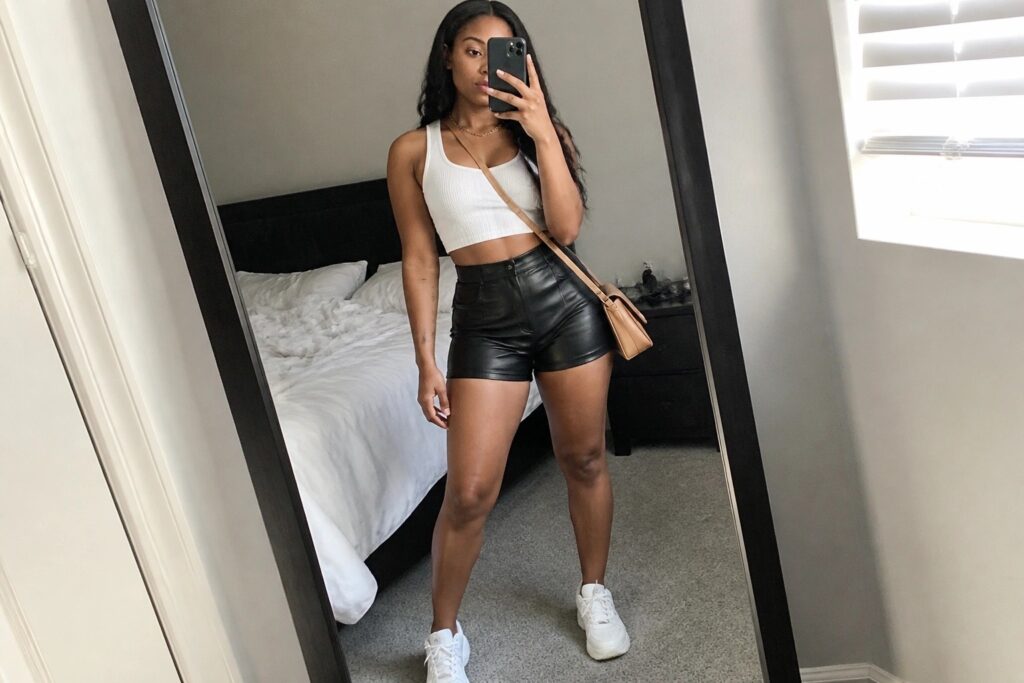 18 Trendy Faux Leather Shorts Outfit Ideas for Black Women Woman in white crop top and black shorts taking bedroom mirror selfie.