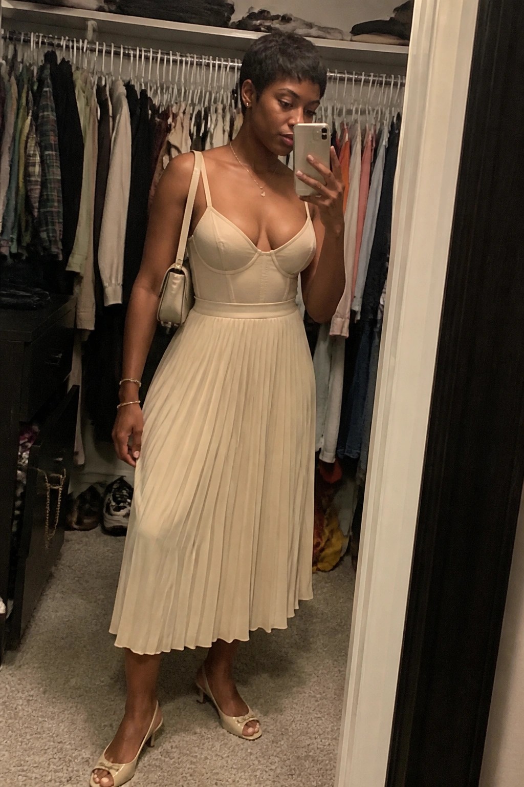 Woman in beige pleated dress taking mirror selfie in walk-in closet