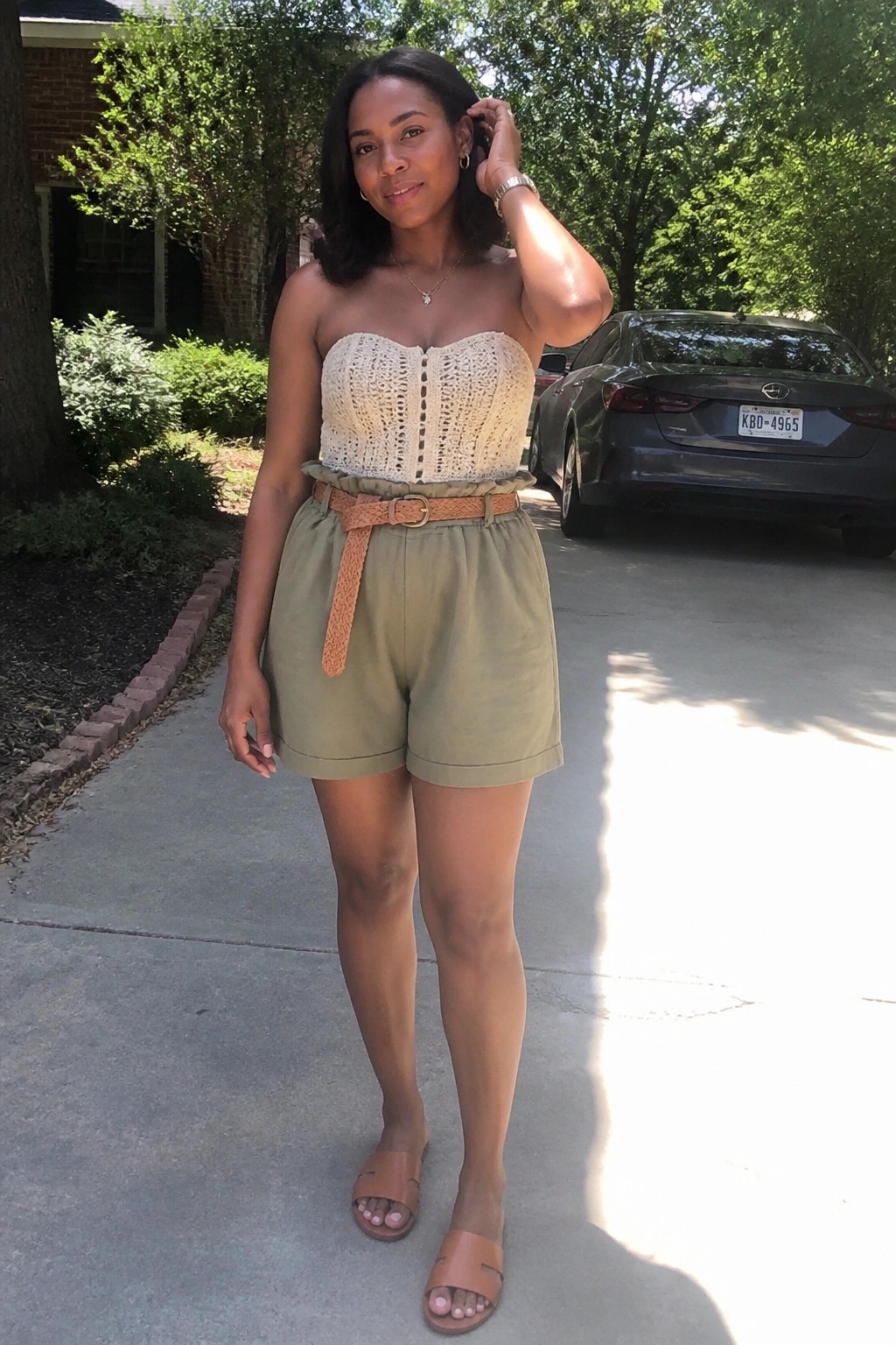 Woman in cream crocheted strapless top and olive shorts with woven belt outdoors