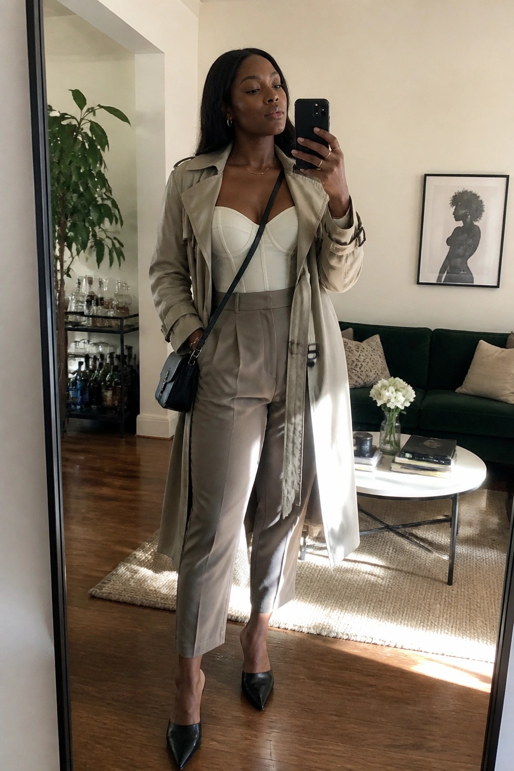 Woman in beige trench coat over white corset and trousers taking mirror selfie