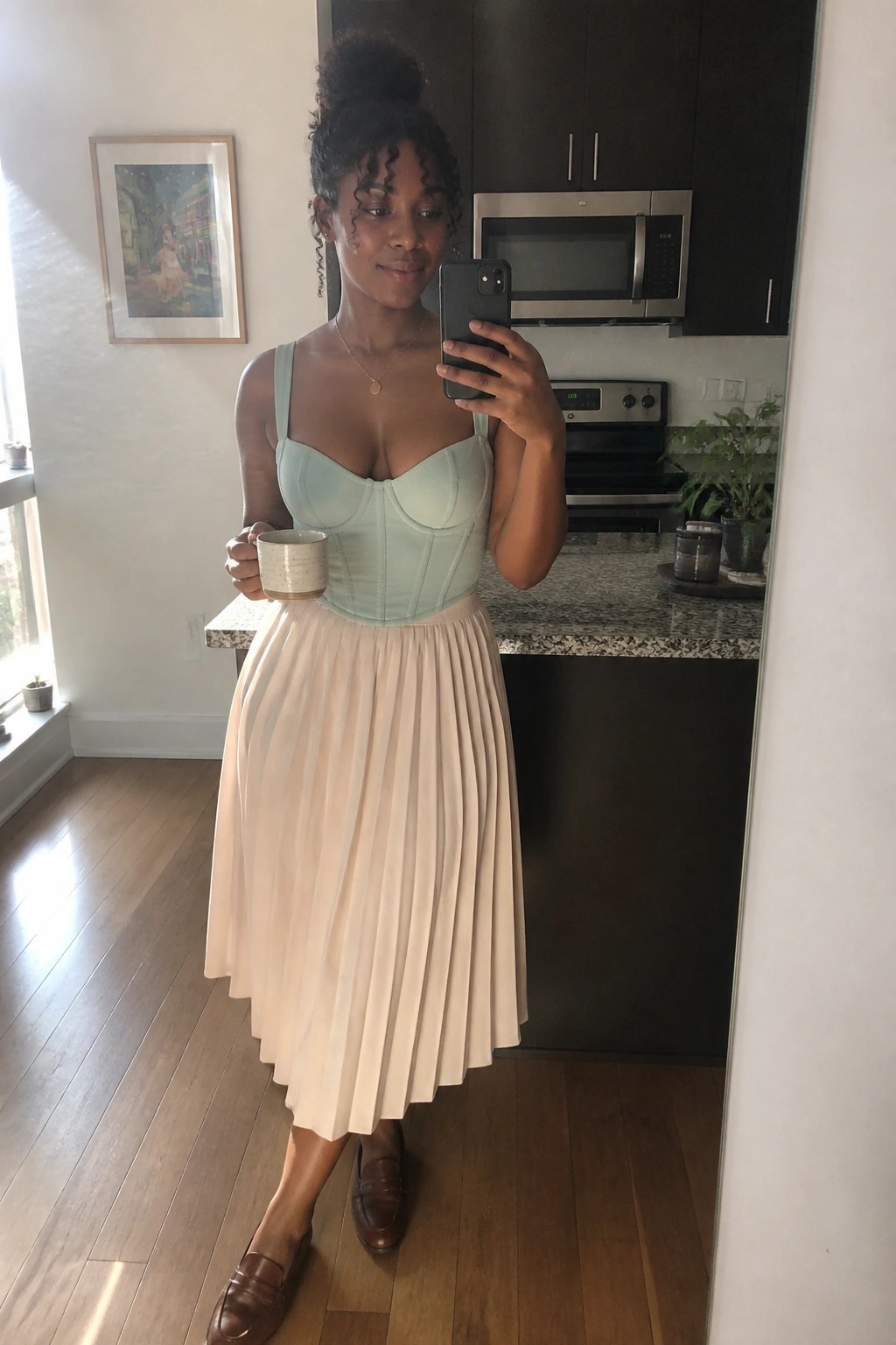 Woman in mint green corset and cream pleated skirt taking kitchen mirror selfie with mug