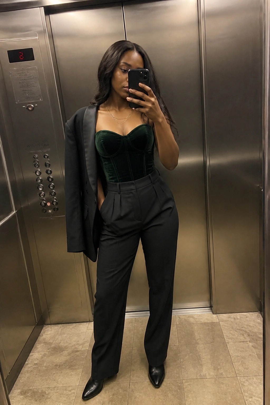 Woman in green velvet corset, black blazer and trousers taking elevator selfie