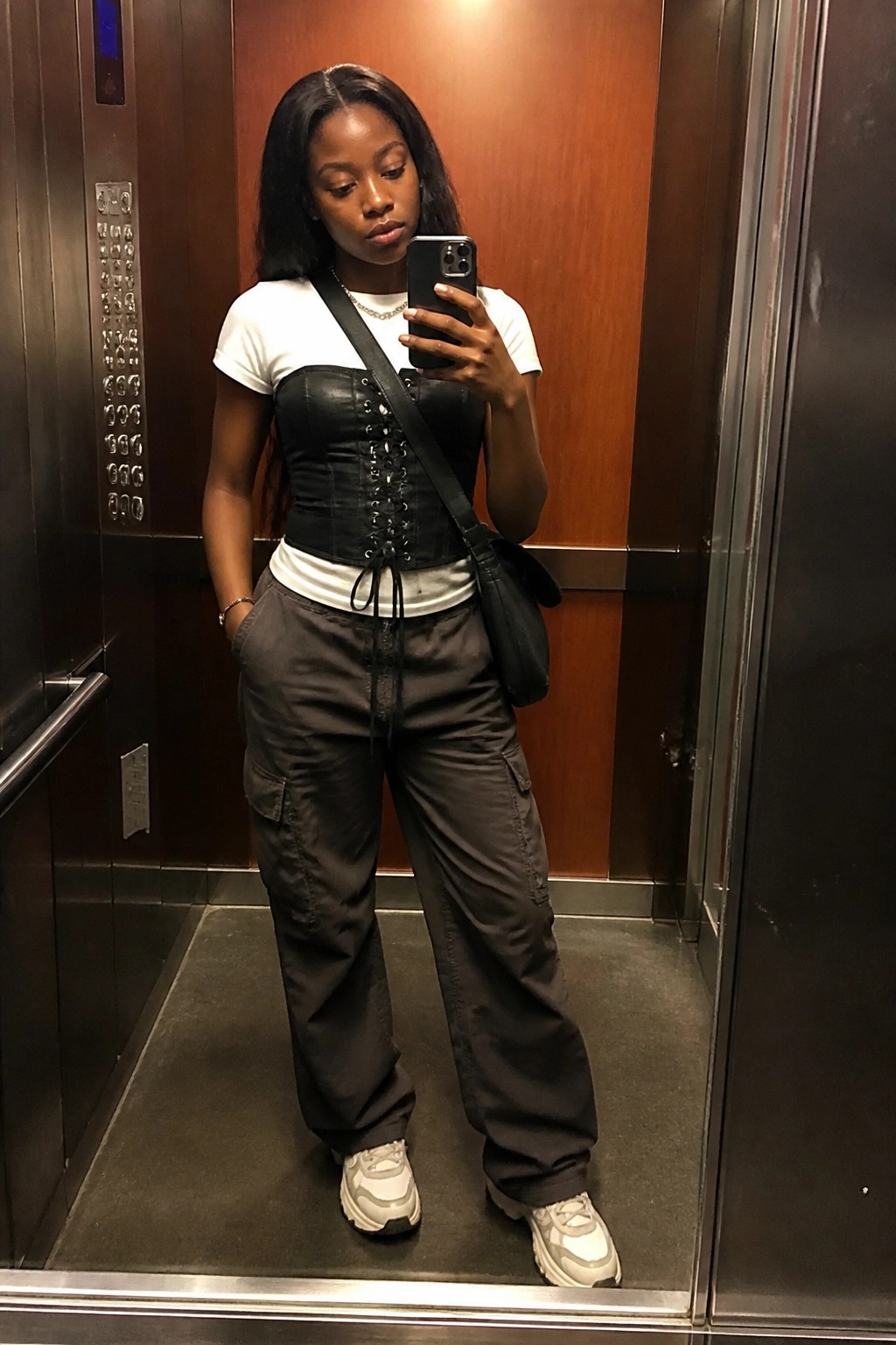Woman taking selfie in elevator wearing black corset and cargo pants