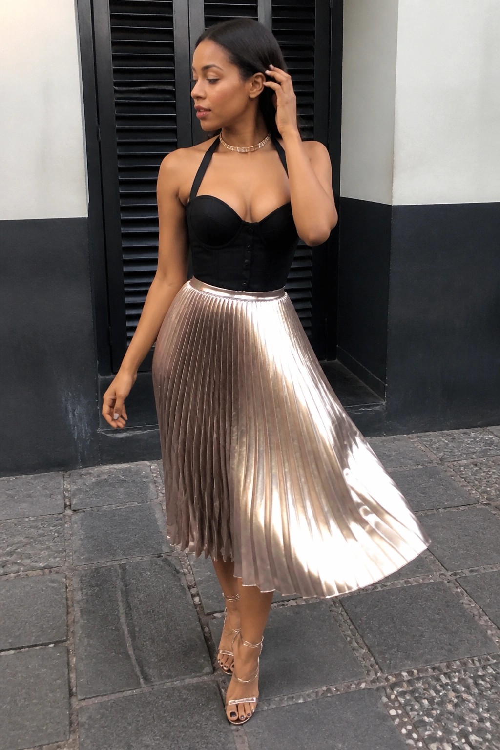 Woman in black halter corset and shiny rose-gold pleated midi skirt with heels