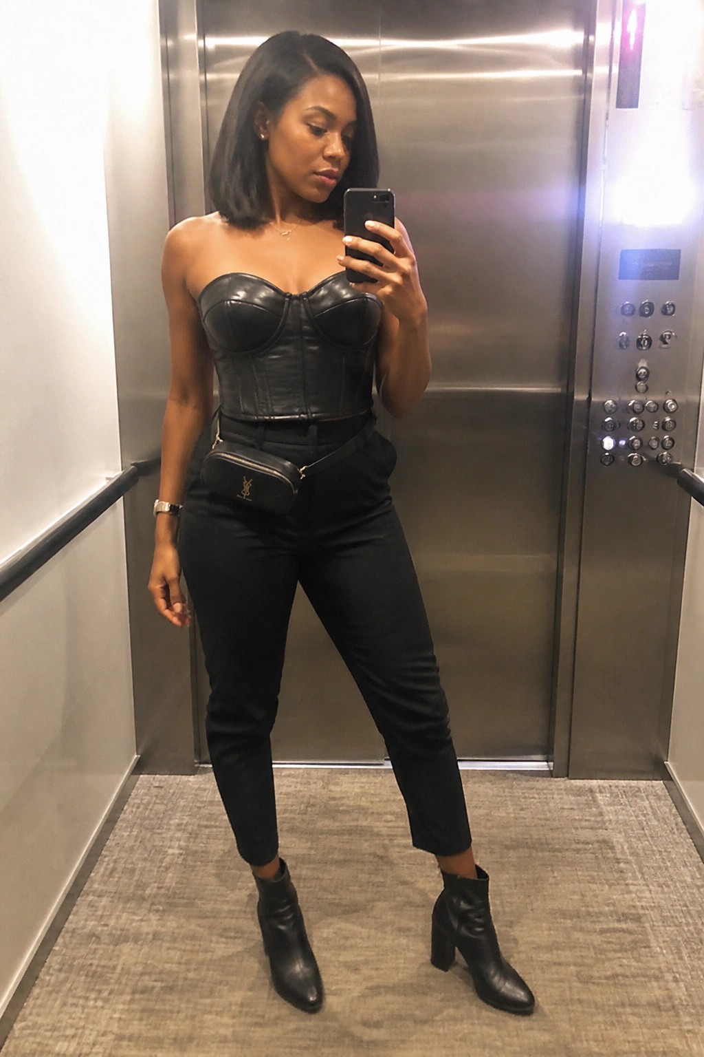 Woman in black leather corset and pants taking selfie in elevator