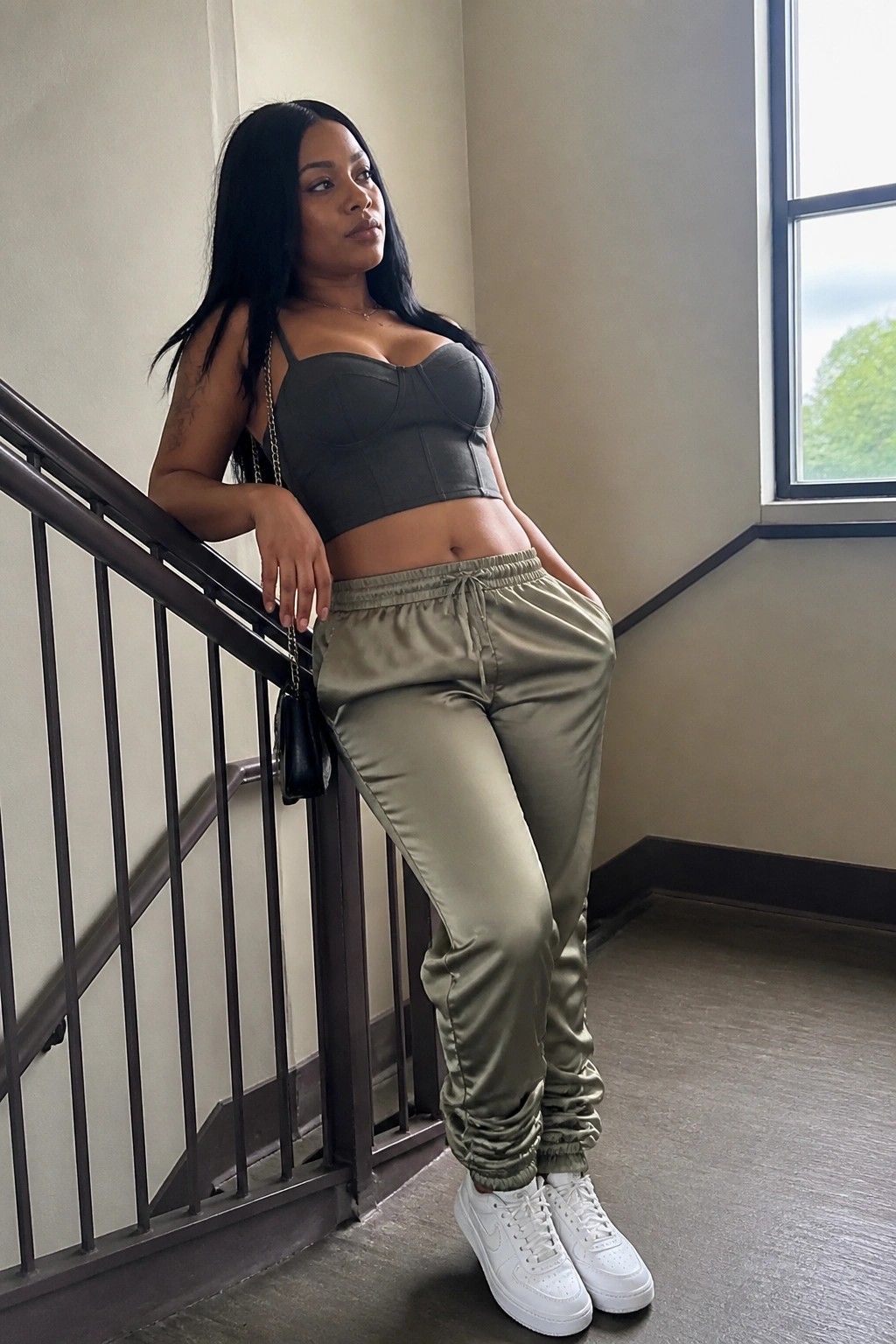Woman with long black hair in grey bustier top and olive satin joggers on stairs