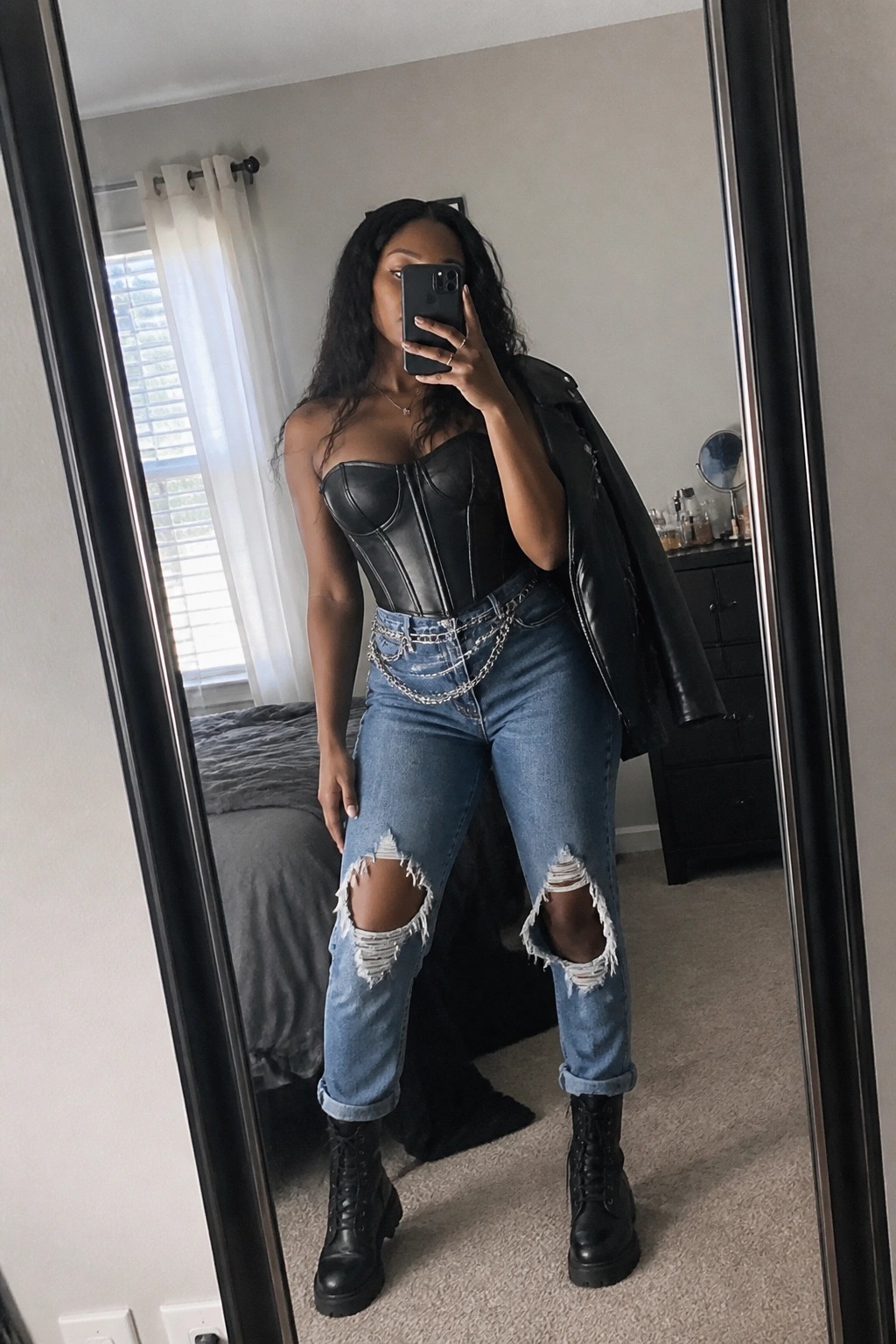 Woman in black corset, ripped jeans with chains, and combat boots taking mirror selfie