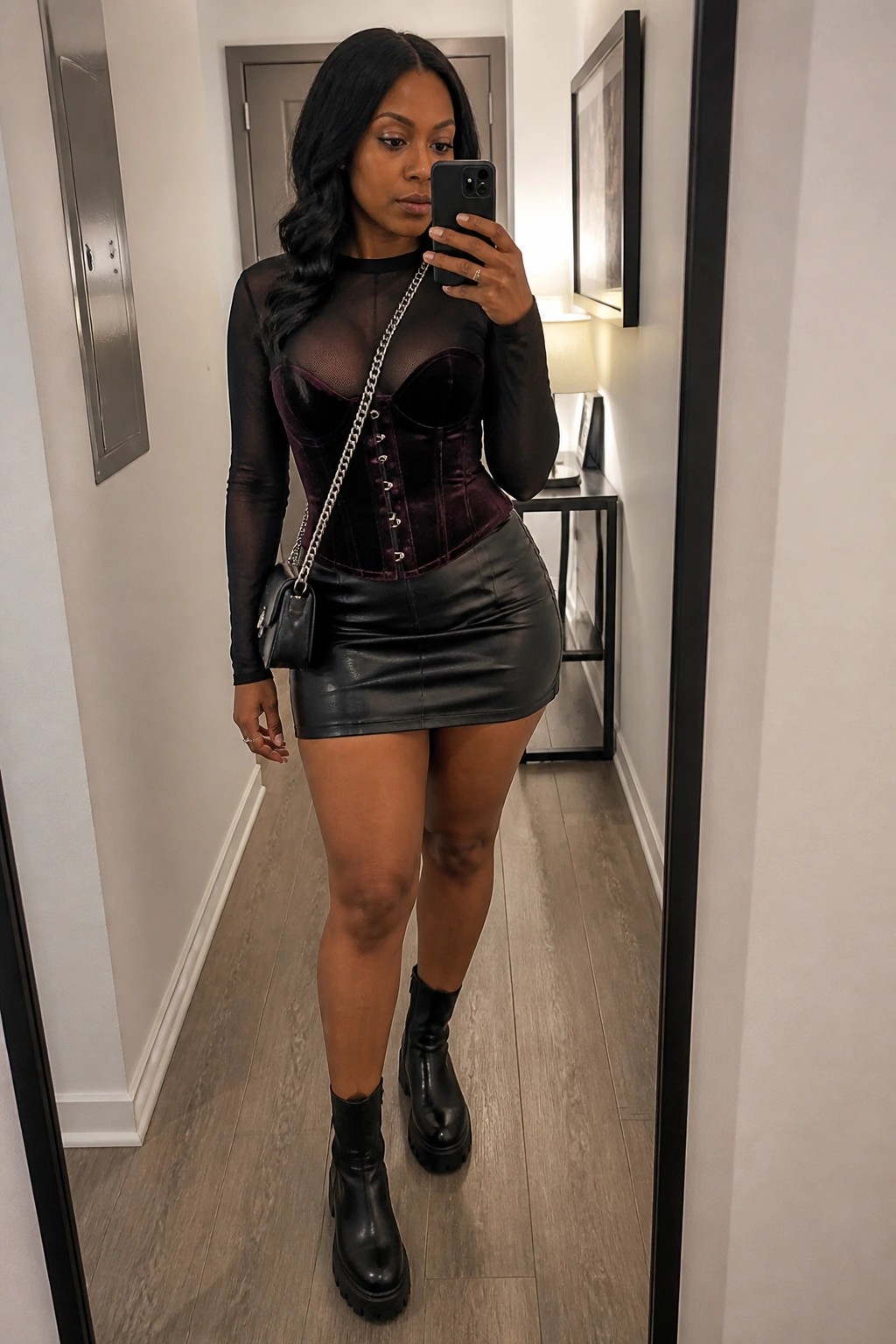 Woman taking mirror selfie in purple velvet corset, black leather skirt, and boots