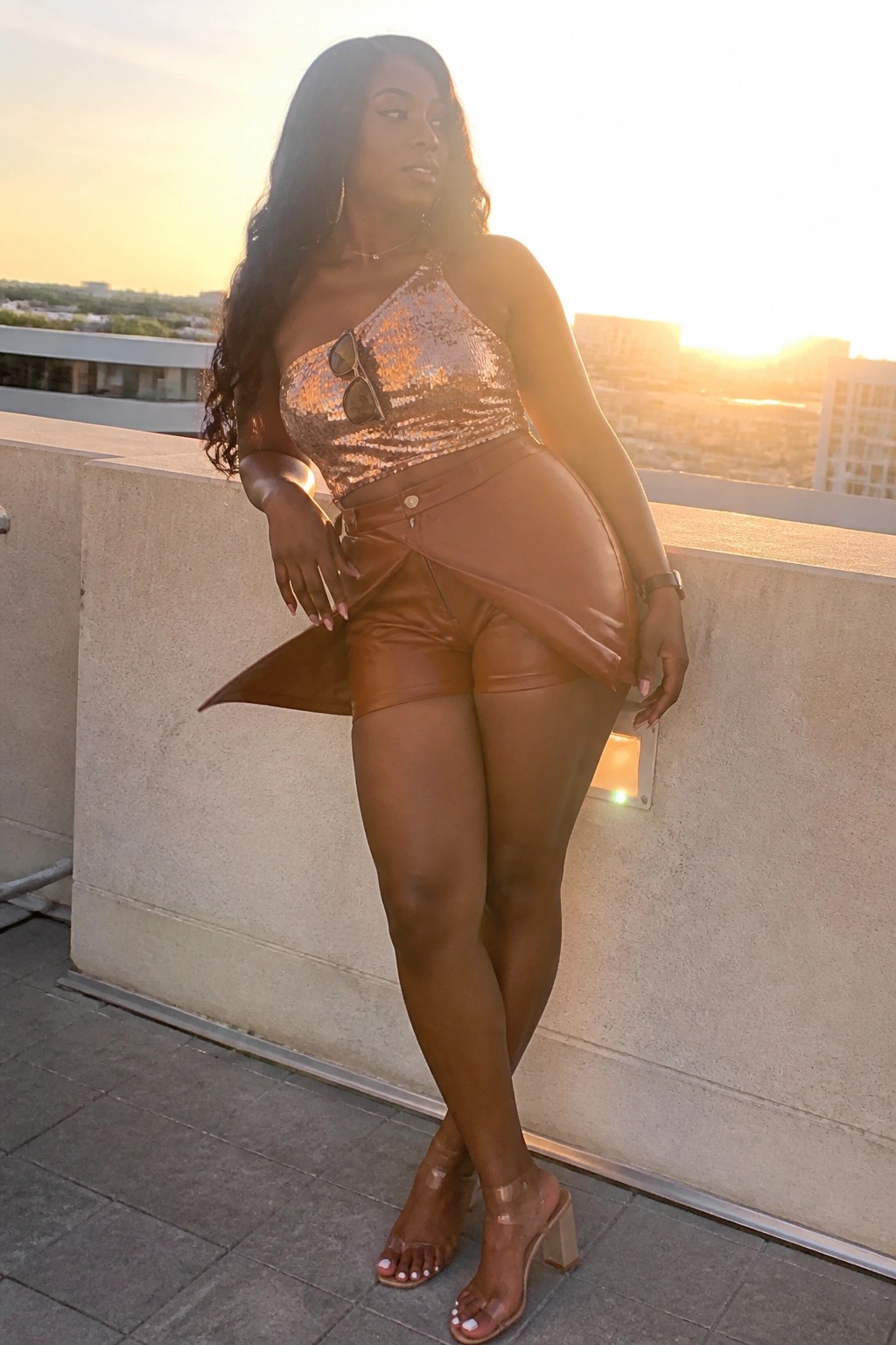 Woman in sequined top and leather shorts posing on rooftop at sunset