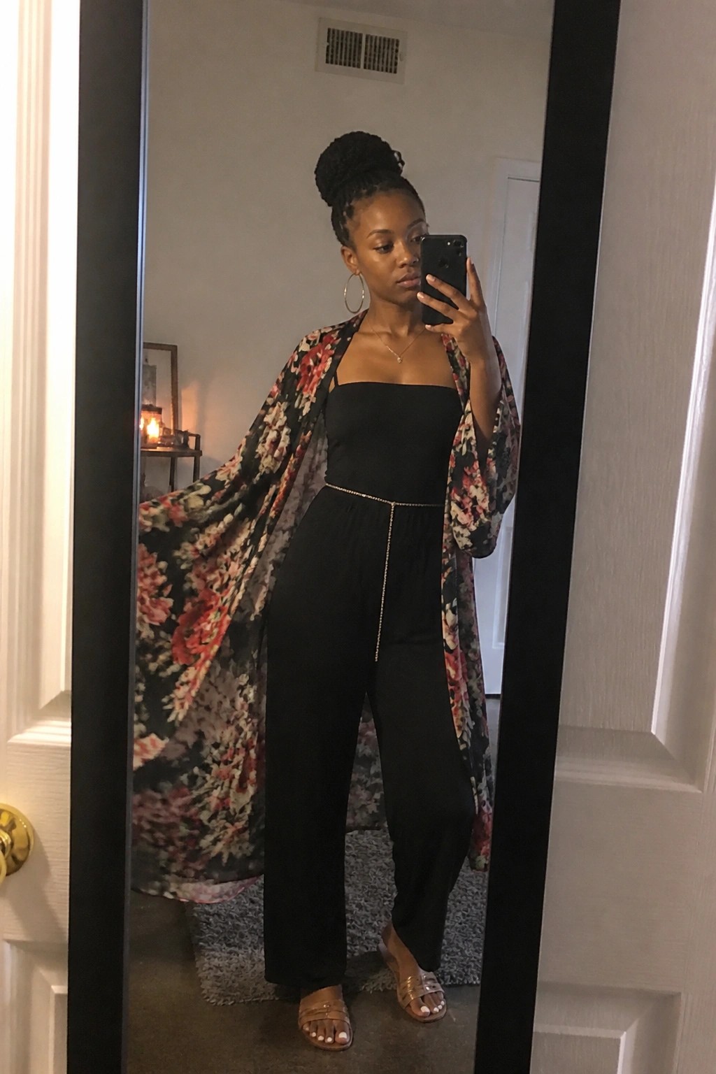 Woman in black jumpsuit and floral kimono taking mirror selfie with phone