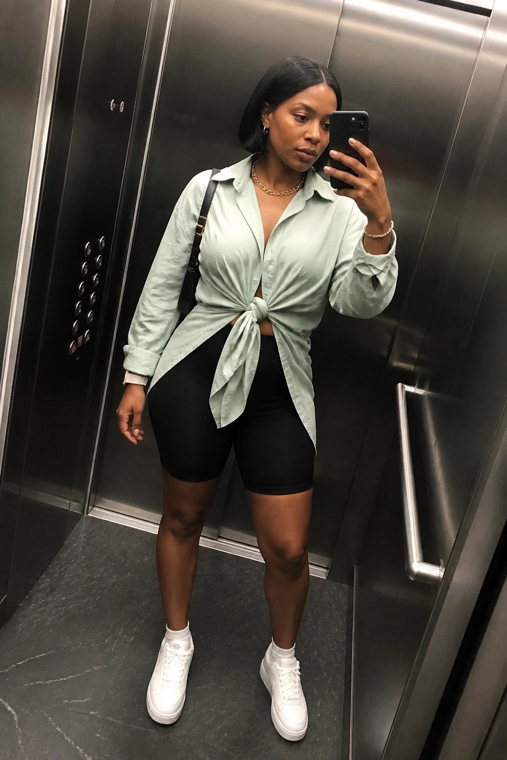 Woman in mint green tied shirt and black shorts taking elevator selfie