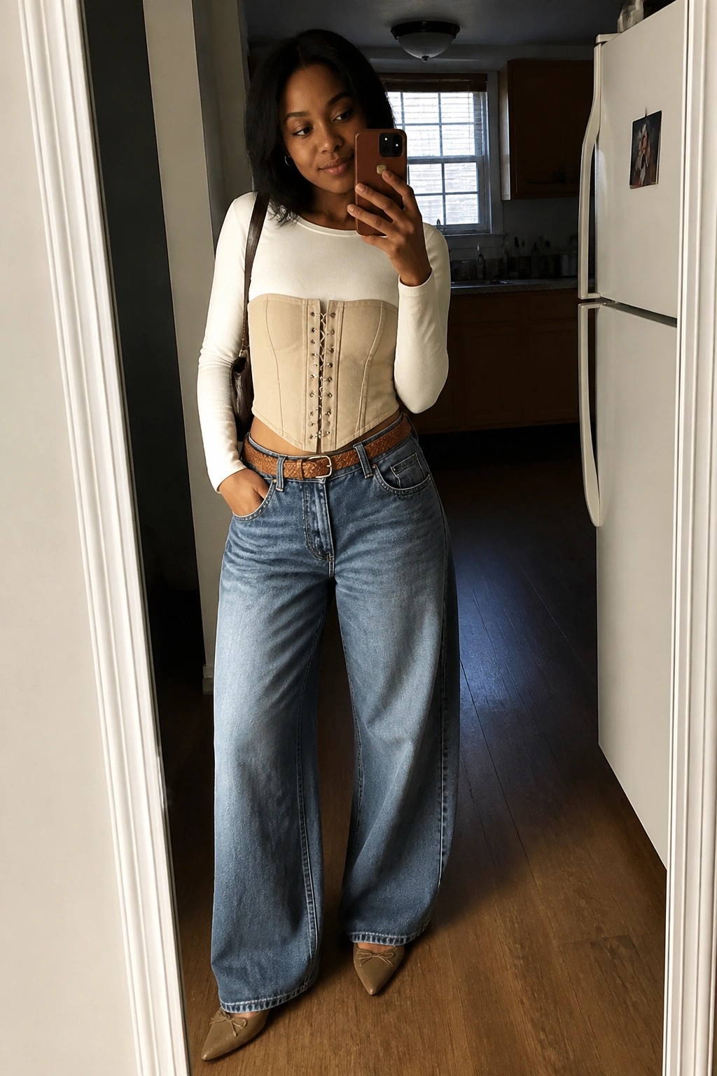 Woman taking mirror selfie in beige corset top, white shirt, and wide-leg jeans.