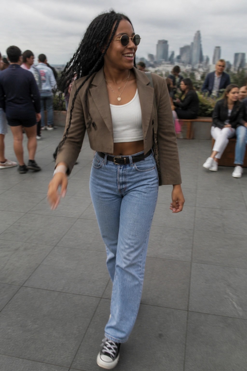 Smiling woman with braids in brown cropped blazer and jeans before city skyline