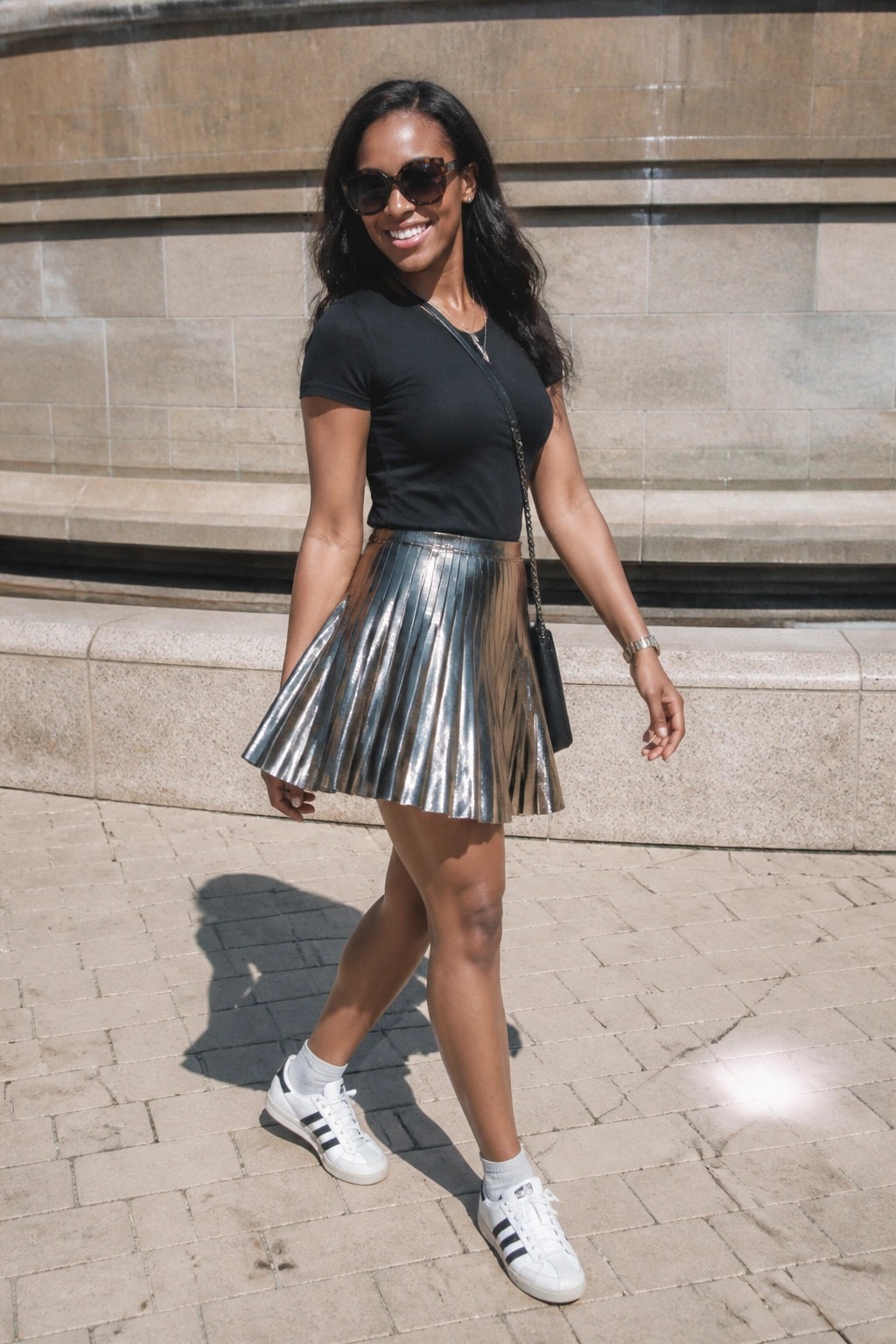 Woman in black top, shiny silver pleated skirt, white sneakers on sunny pavement
