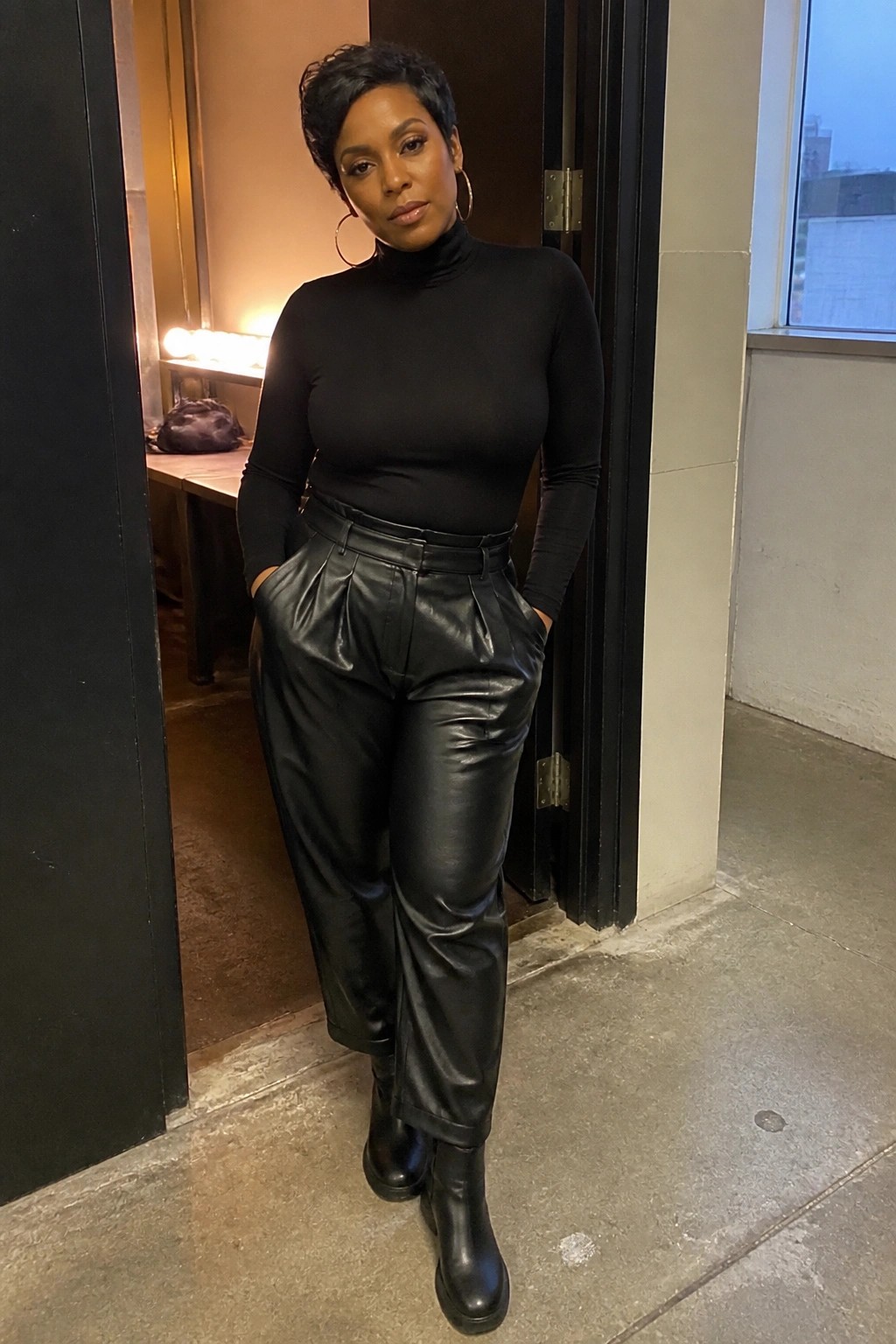 Woman in black turtleneck and pleated leather pants standing in doorway.