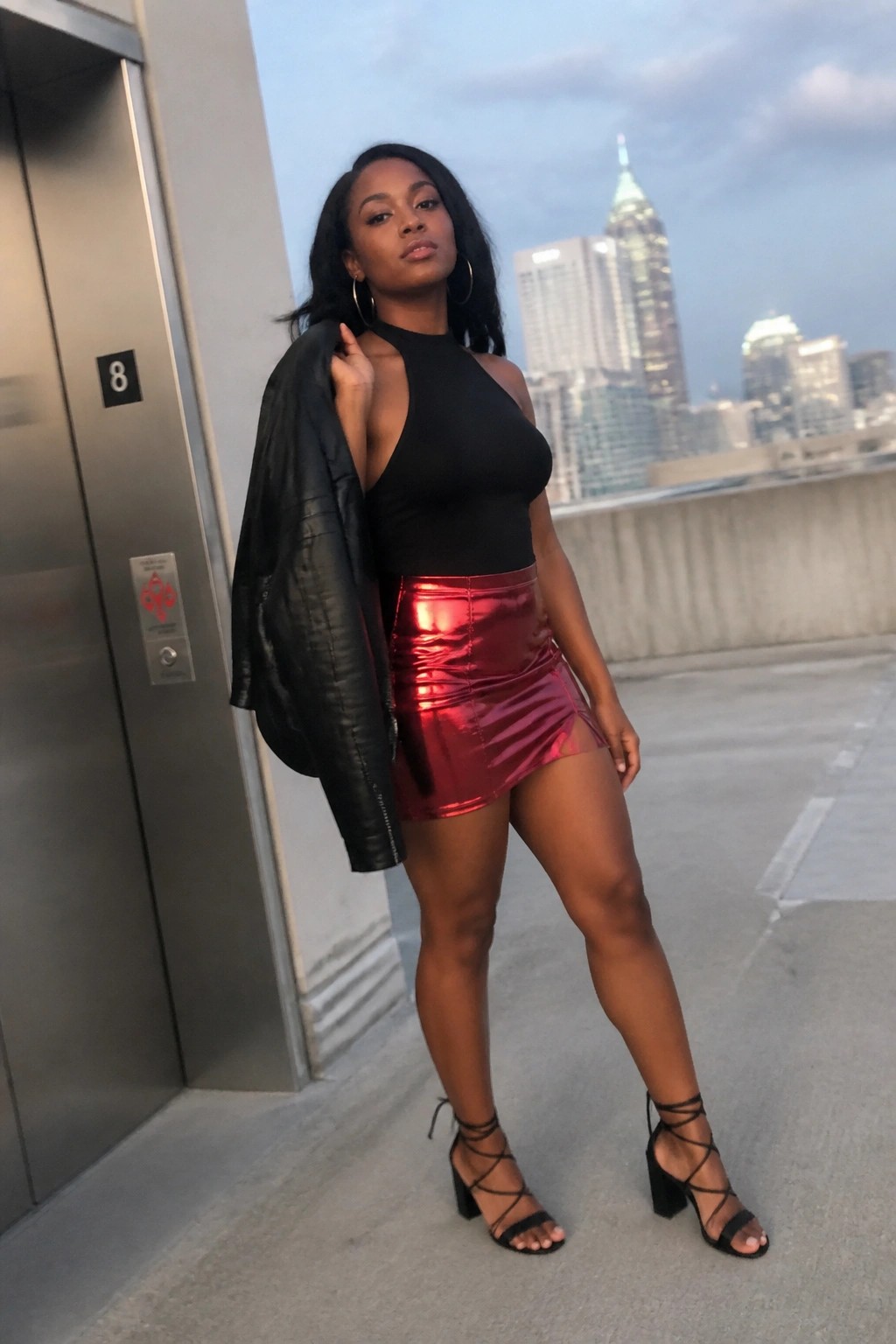 Woman in black halter top and shiny red mini skirt on city rooftop