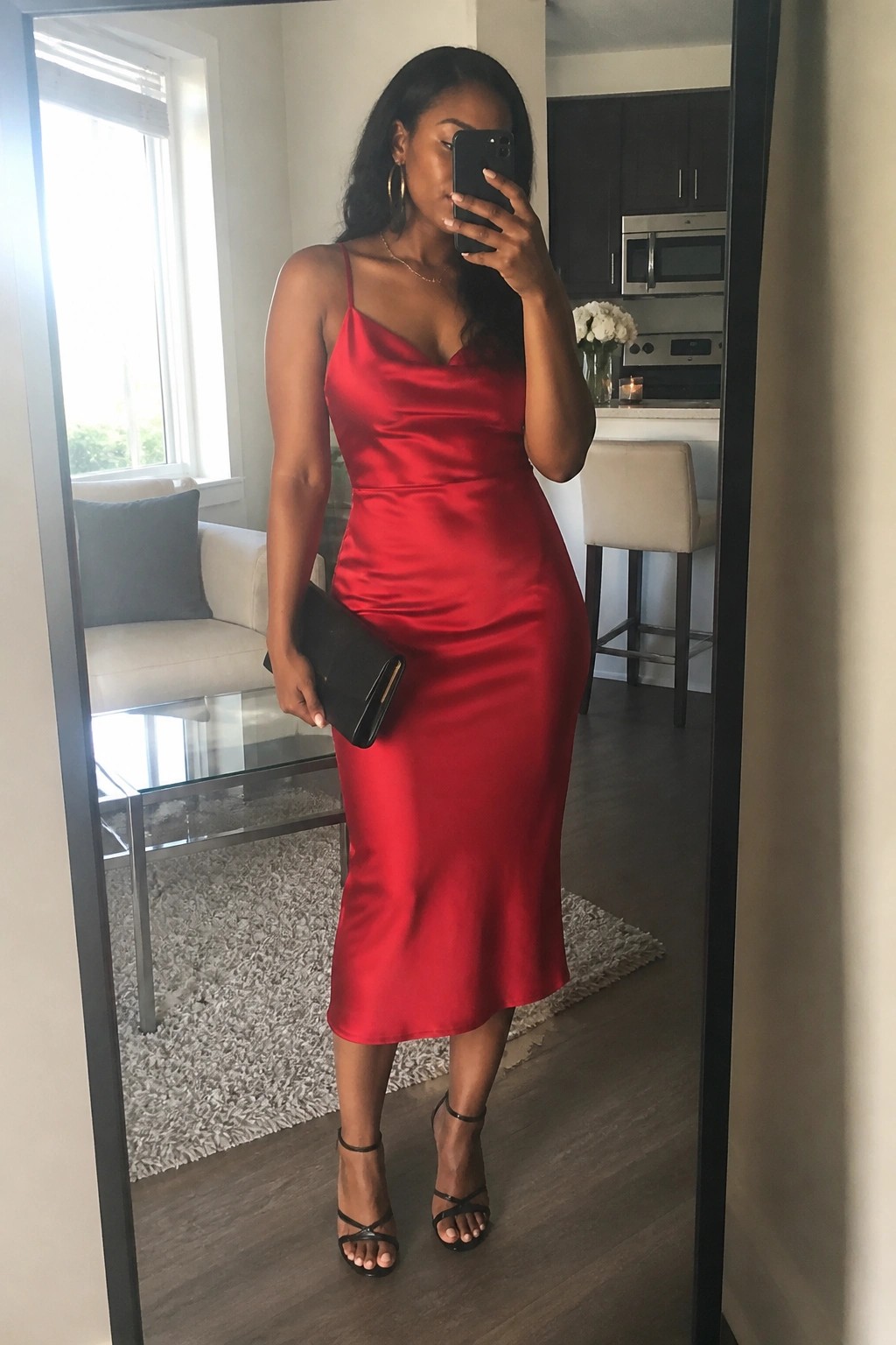 Woman in red satin midi dress taking mirror selfie with phone and clutch