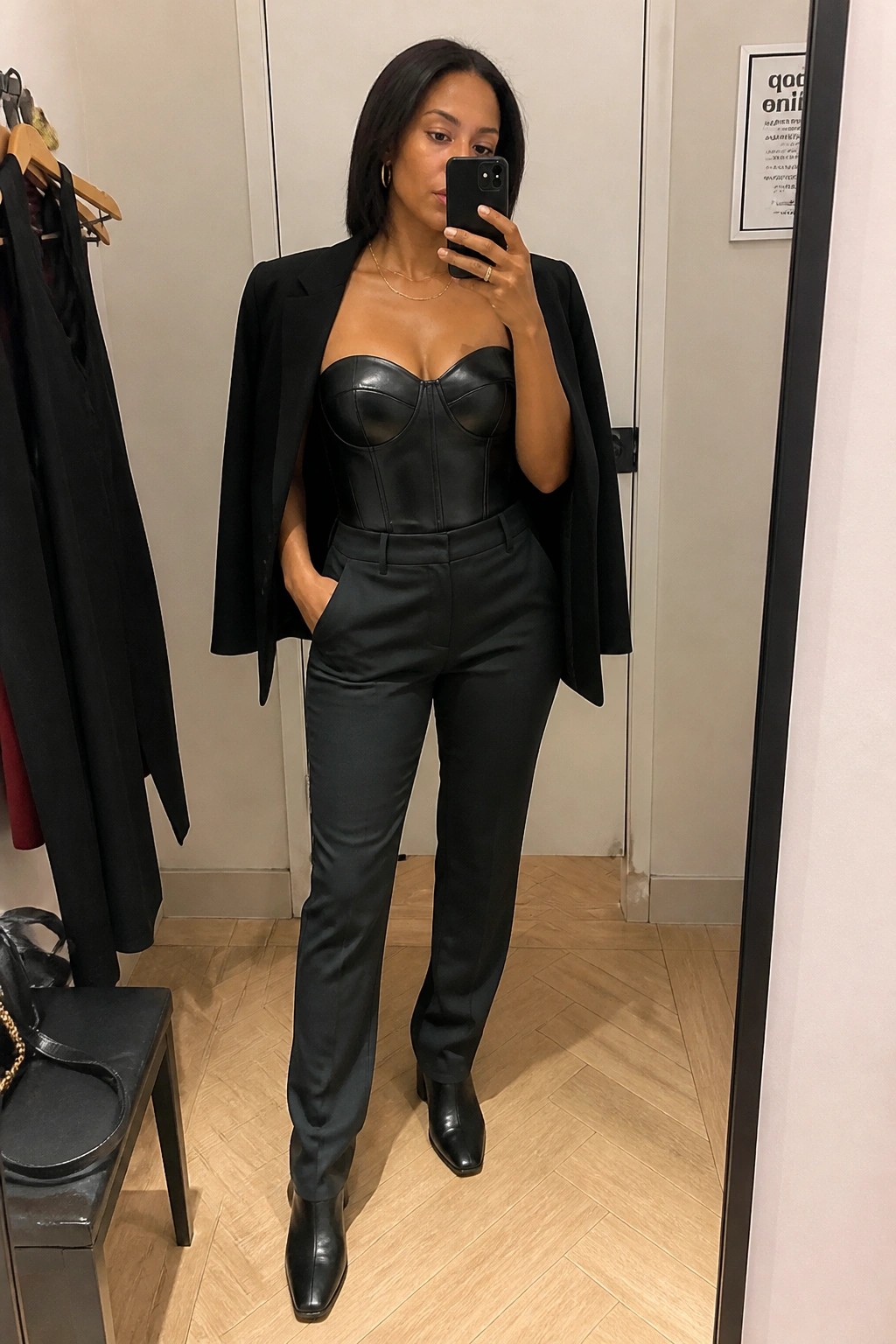 Woman in black corset top and blazer taking mirror selfie in fitting room
