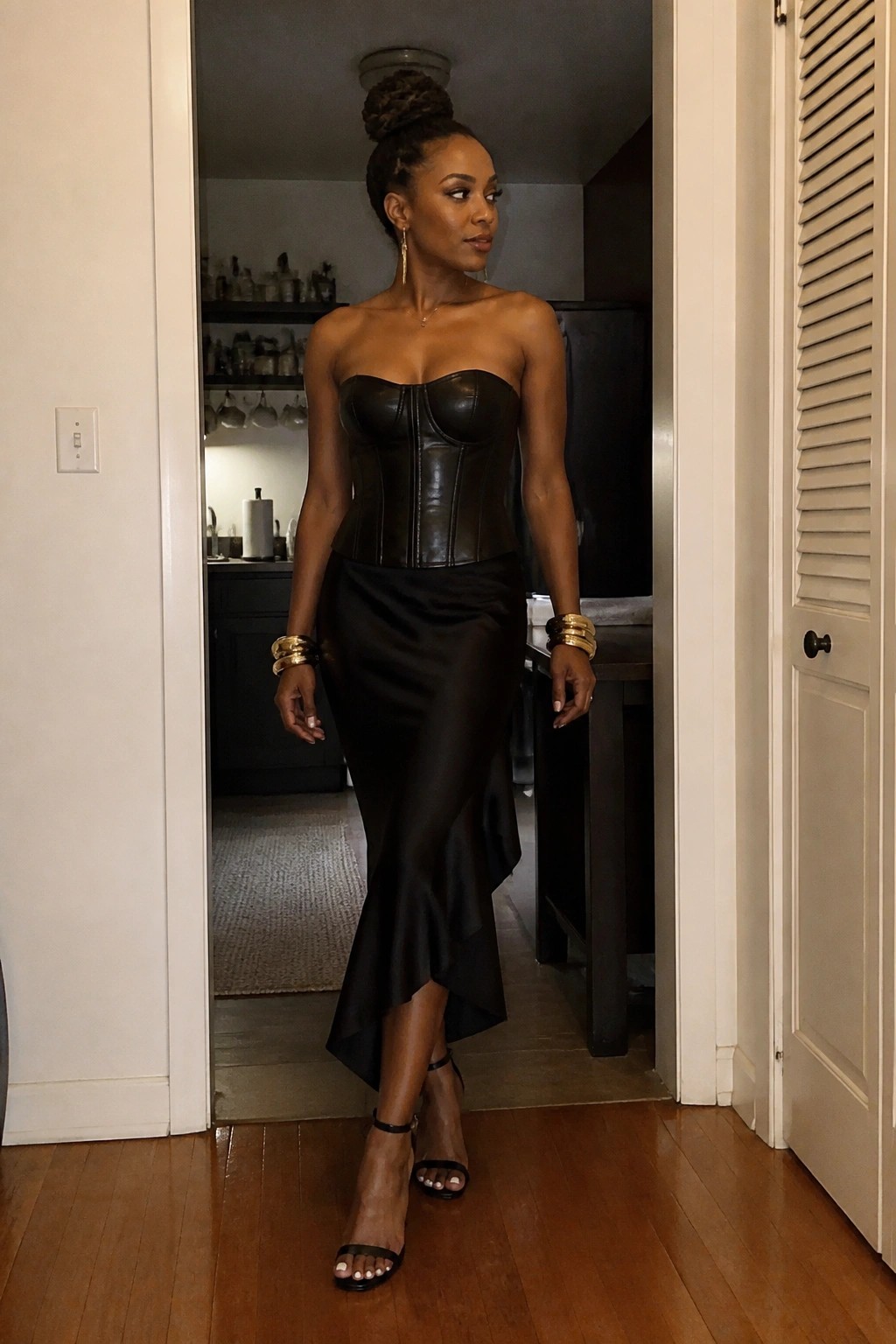 Woman in black strapless corset and asymmetrical satin skirt with gold jewelry in doorway