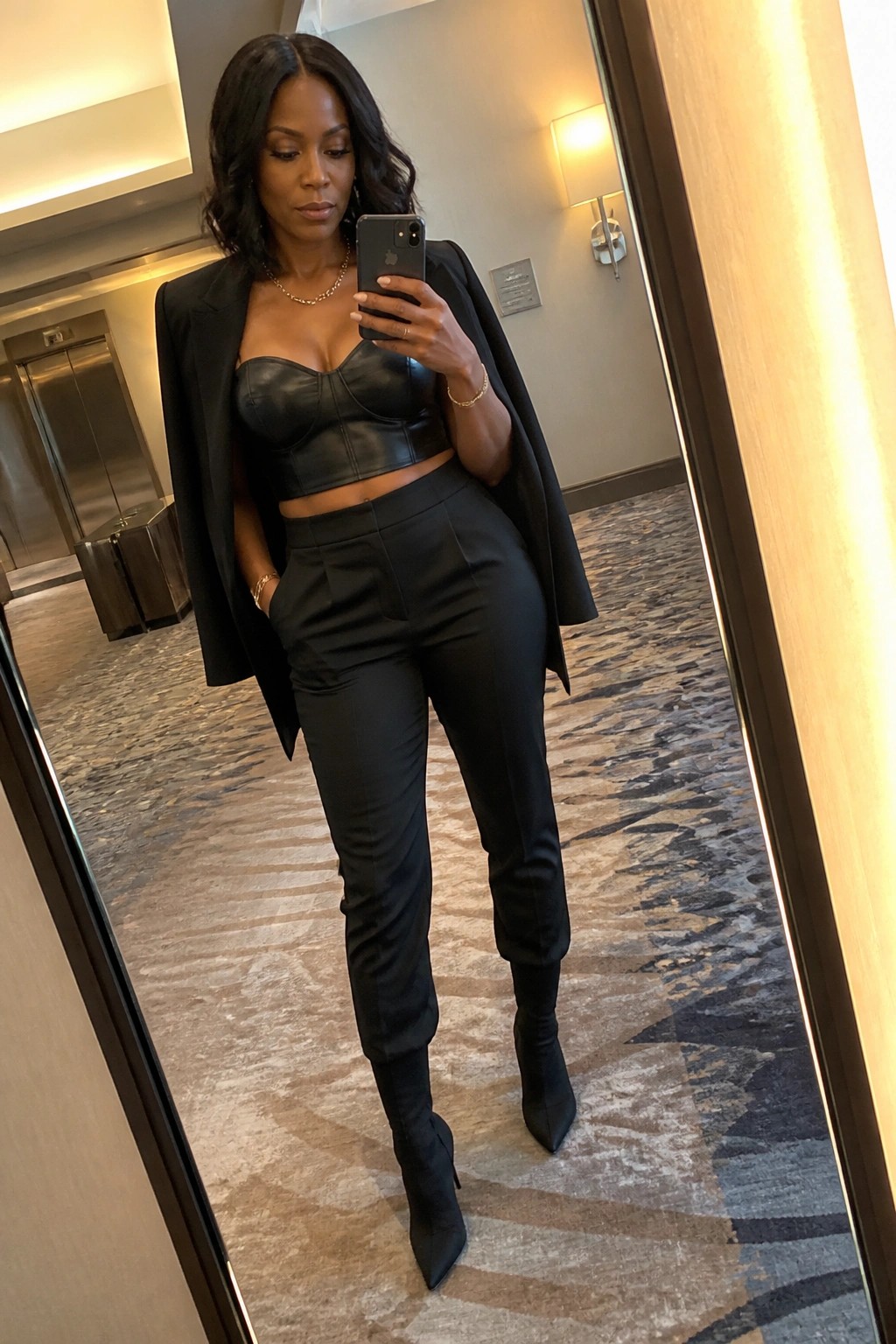 Woman in black blazer and crop top takes mirror selfie in hallway