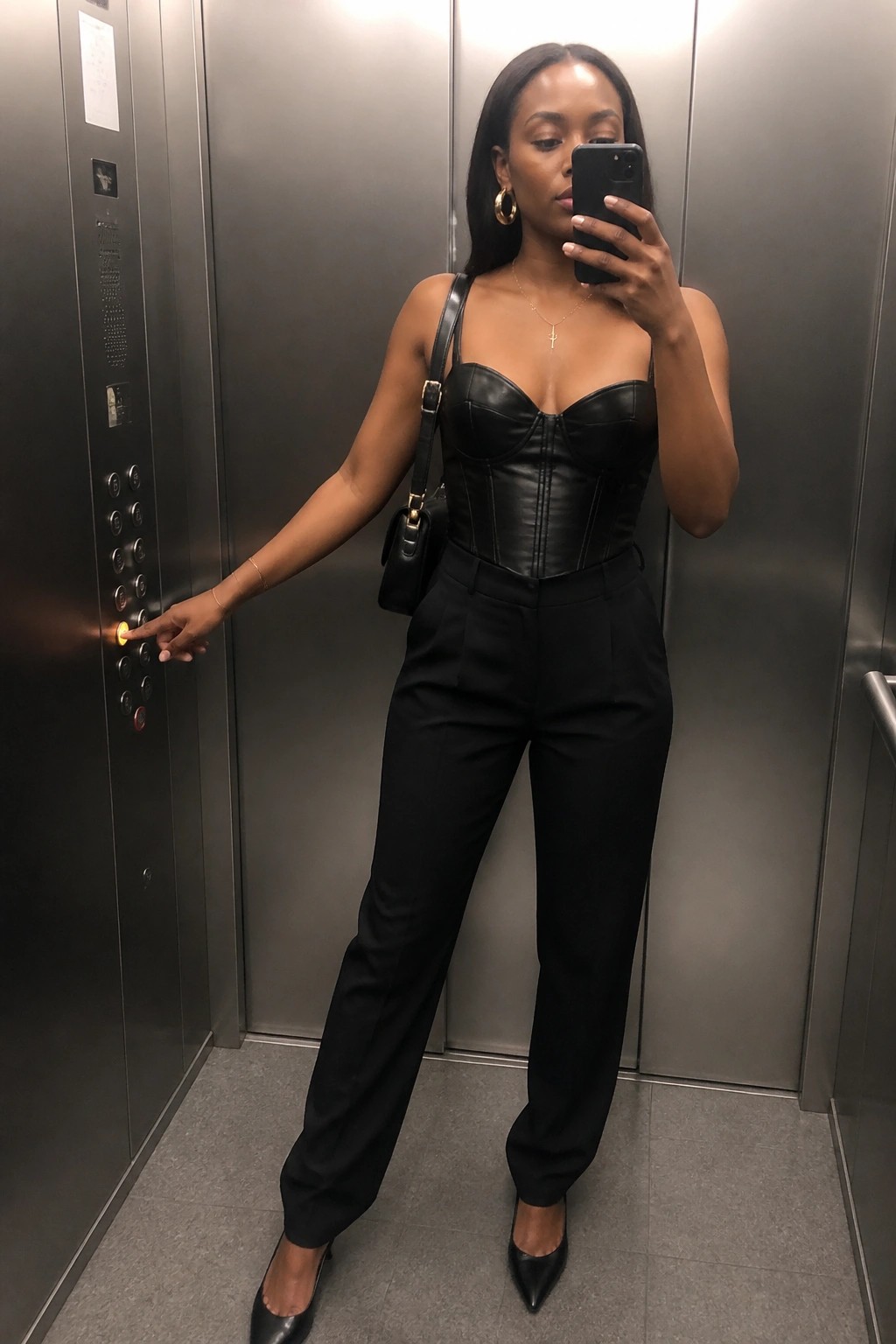 Woman in black corset and pants pressing elevator button while taking selfie