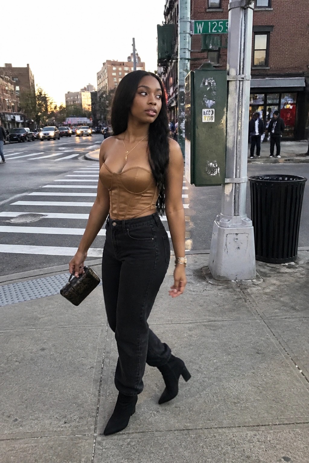 Woman in brown corset top and black jeans on city sidewalk holding handbag
