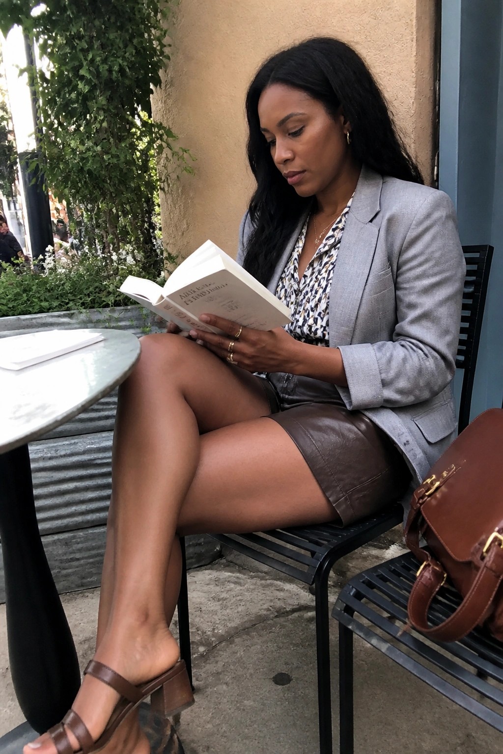 Woman in gray blazer and brown leather skirt reads Alice's Adventures in Wonderland outdoors.