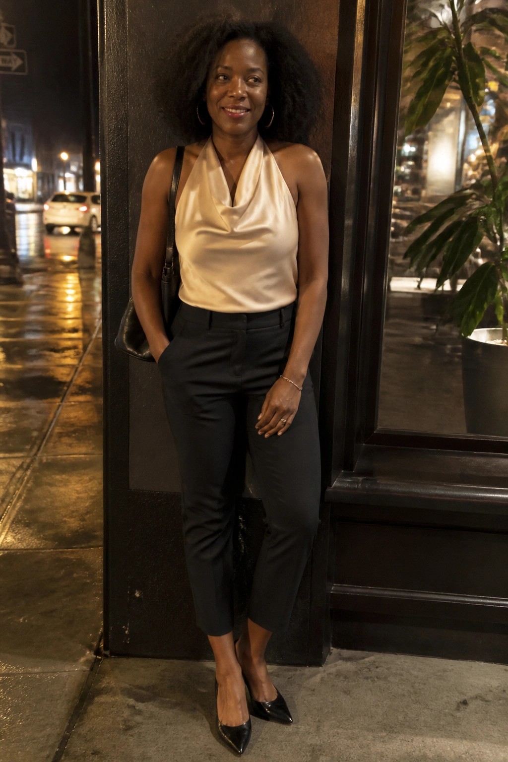 Woman with curly afro in beige satin halter top and black pants on city street at night