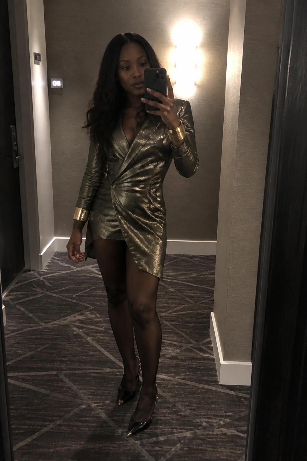 Woman in metallic gold dress takes mirror selfie in hallway