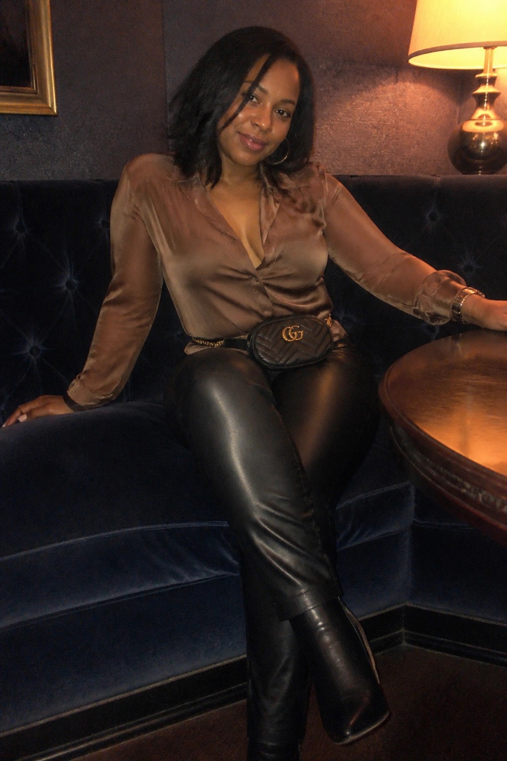 Woman in brown satin blouse and black leather pants on blue velvet couch with Gucci bag.
