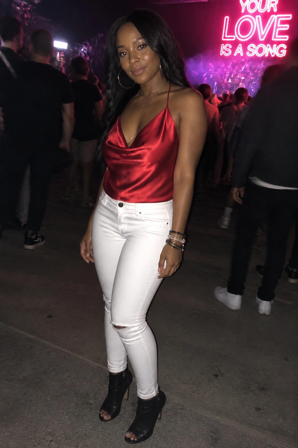 Woman in red satin top and white ripped jeans at nightclub with neon sign