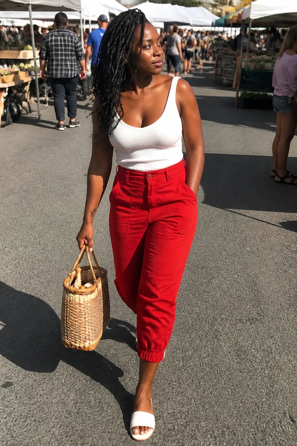 Woman in white tank top and red pants holding woven basket at outdoor market