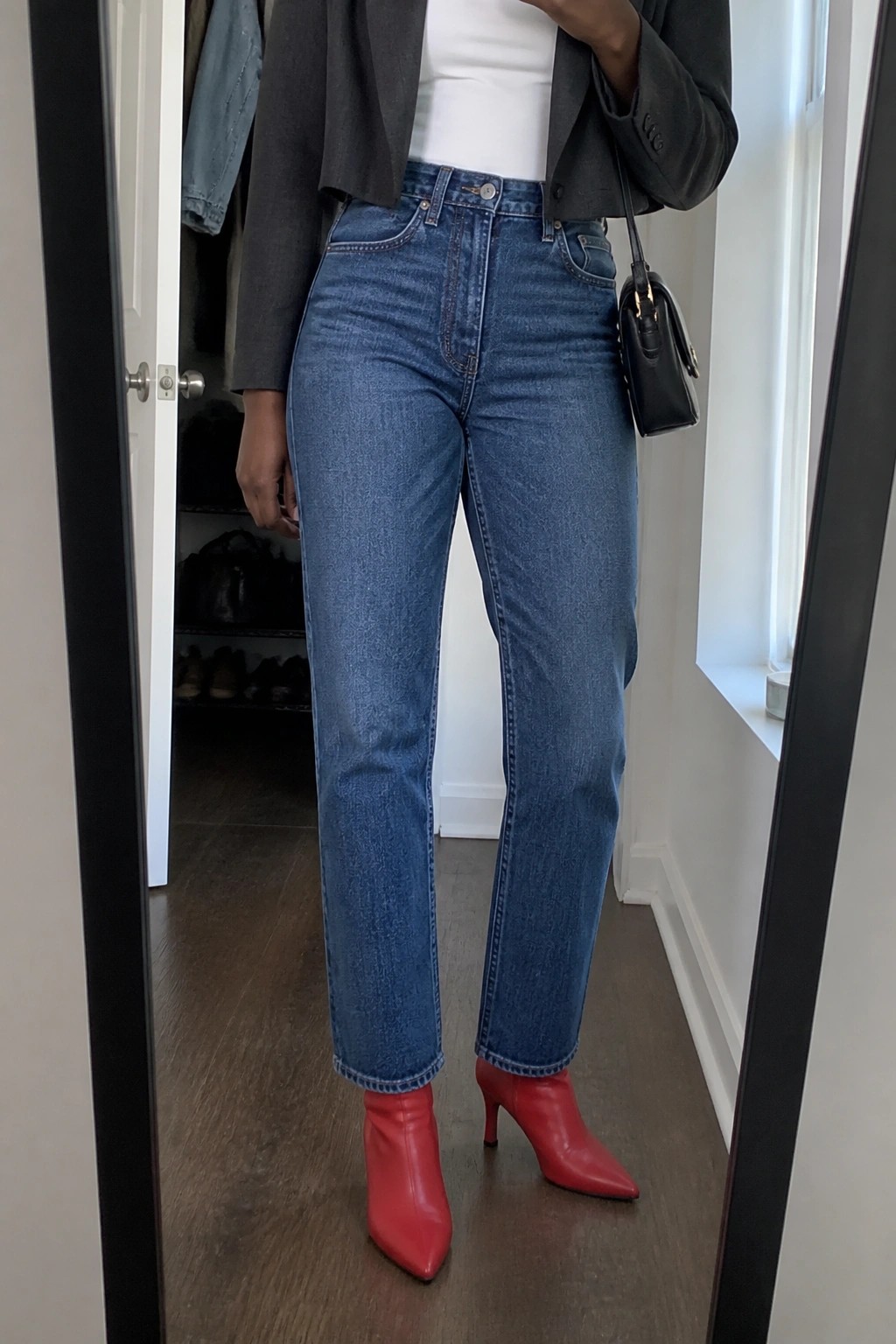 Woman in blue jeans, red pointed-toe boots, gray blazer, and black purse.