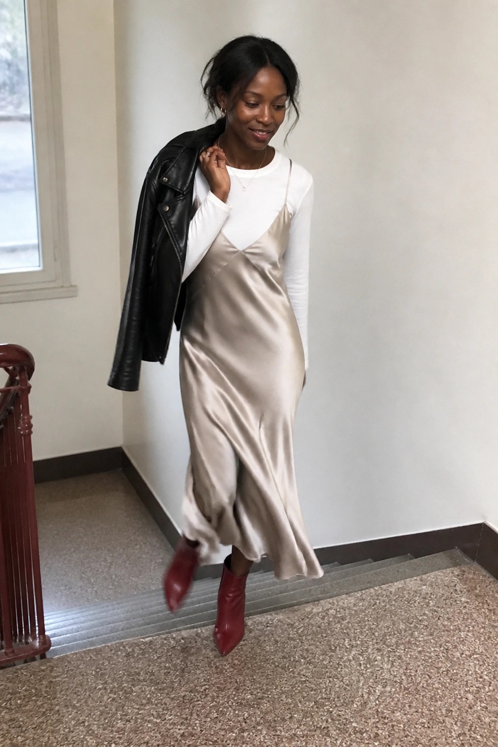 Woman in beige satin slip dress, white top, red boots, holding black leather jacket on stairs