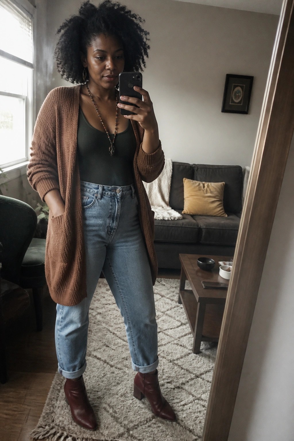 Woman in brown cardigan over green top with jeans and boots takes mirror selfie