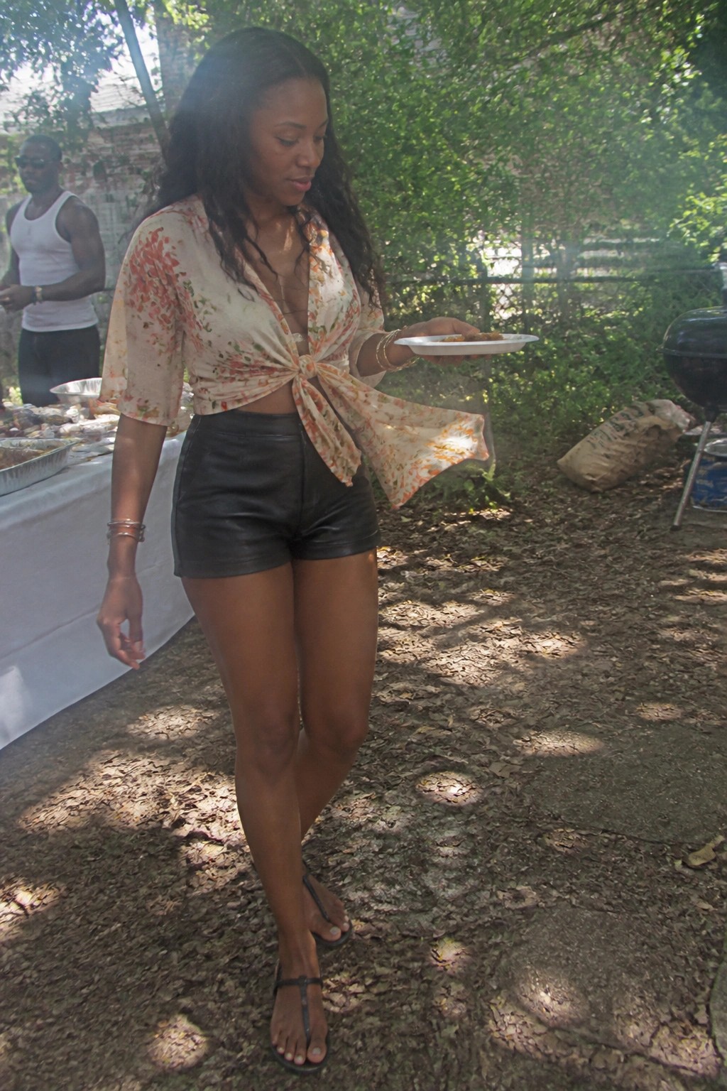 Woman in floral tie-front top and leather shorts holding plate at outdoor cookout