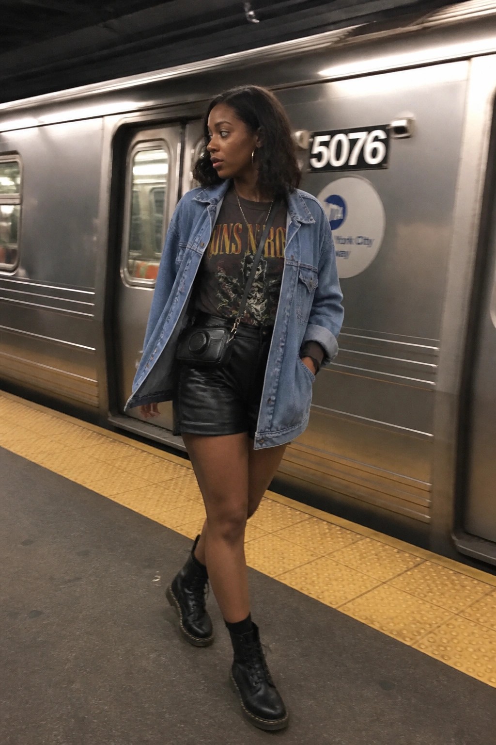 Woman in denim jacket and leather shorts stands by subway train
