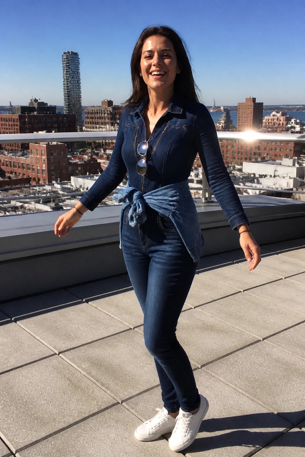 Smiling woman in blue denim outfit and white sneakers on sunny city rooftop