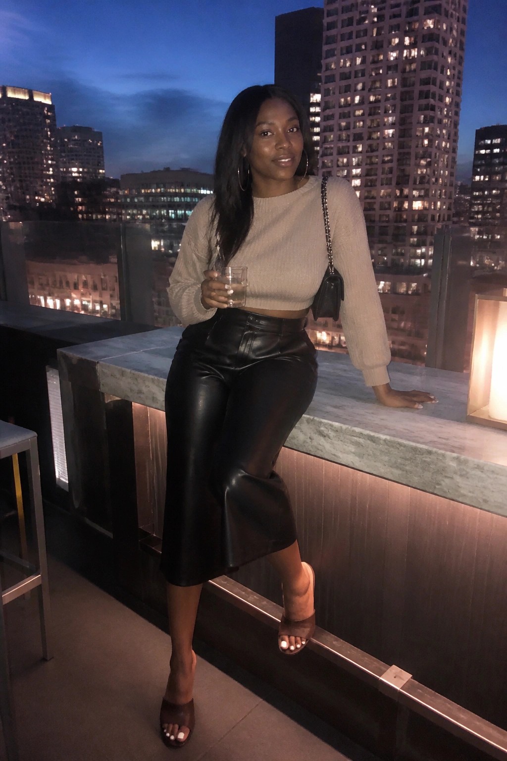Woman in beige crop sweater and black leather skirt on city balcony at night