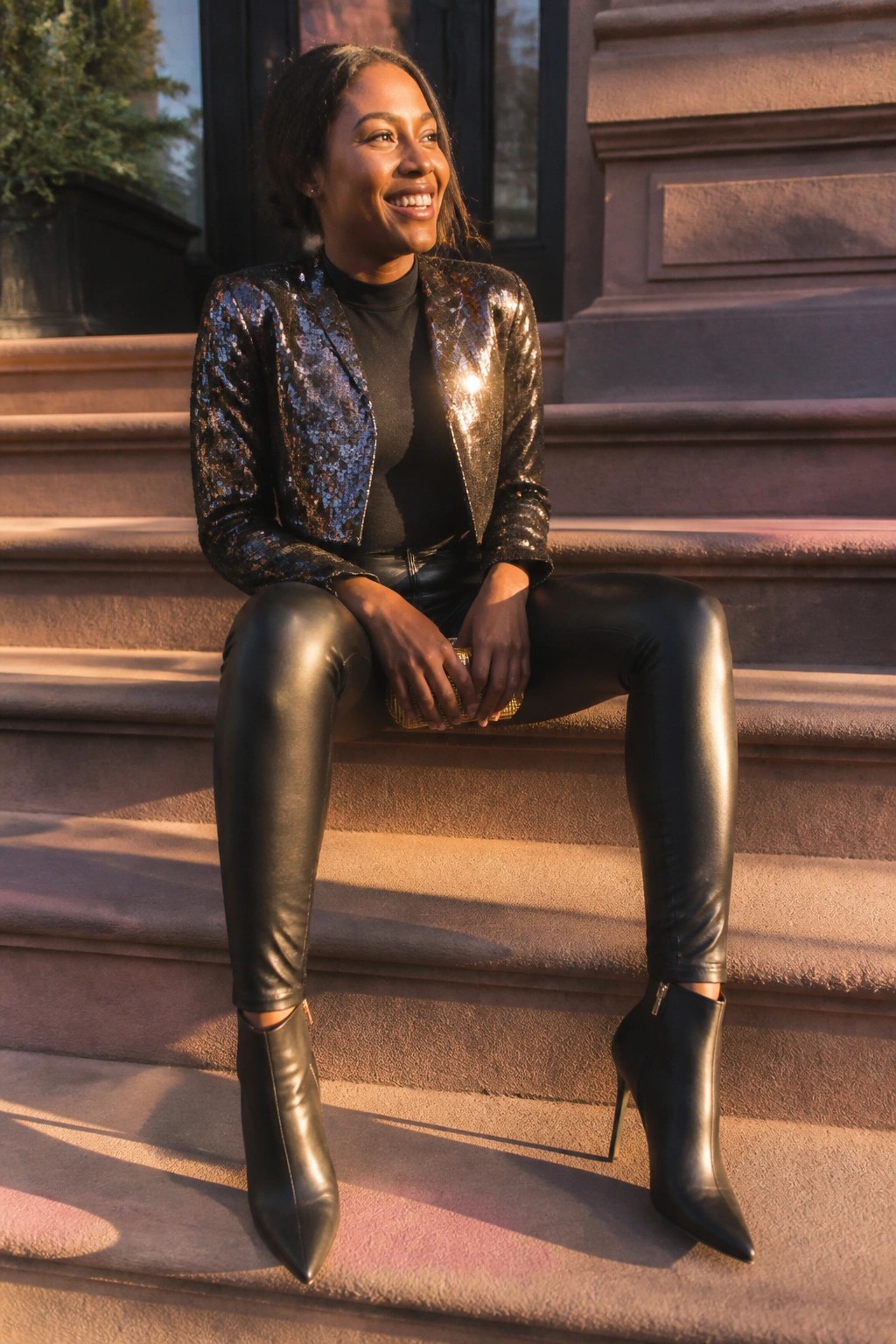 Smiling woman in sequined jacket and black leather pants on stone steps