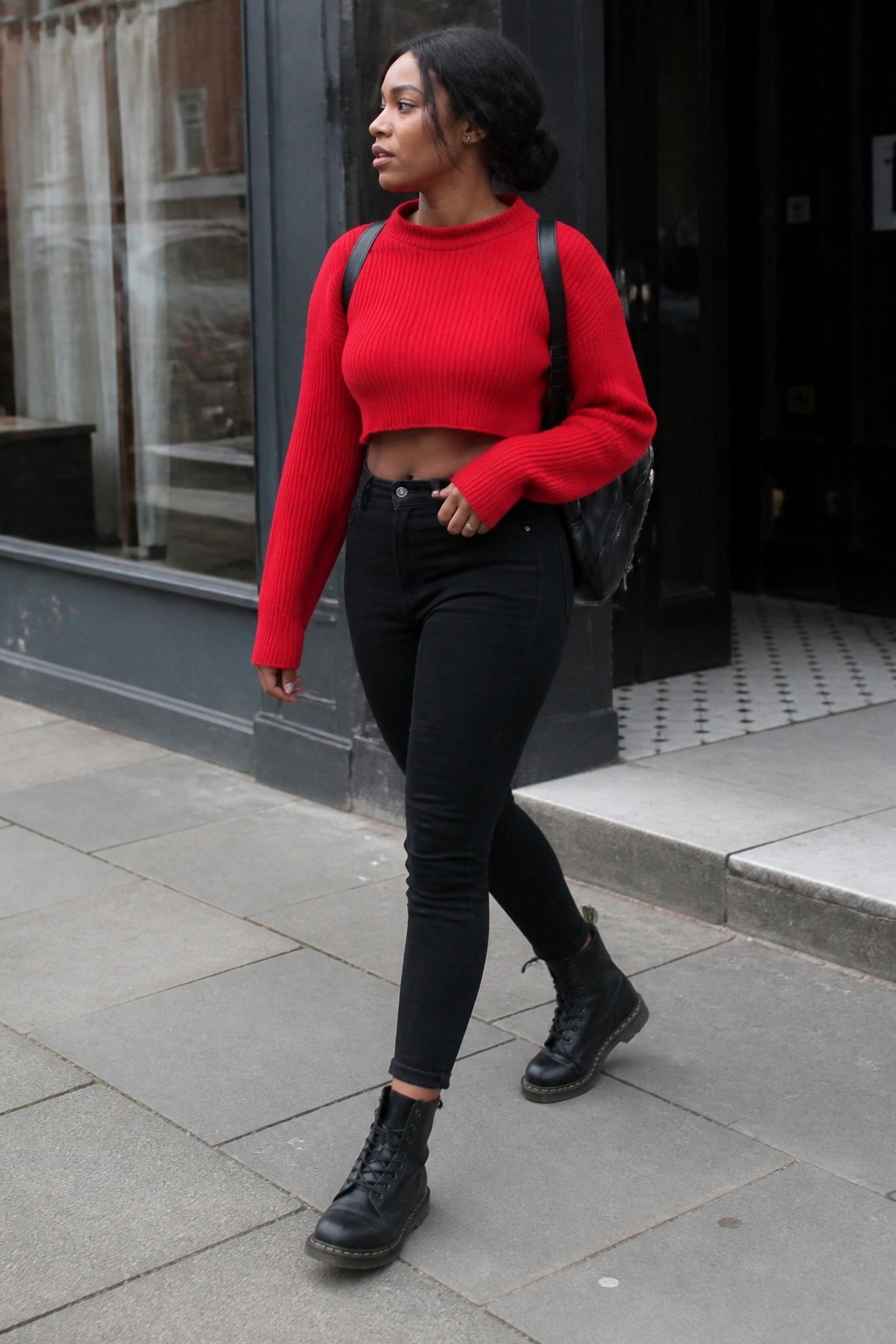 Woman in red cropped sweater and black jeans walking on city sidewalk